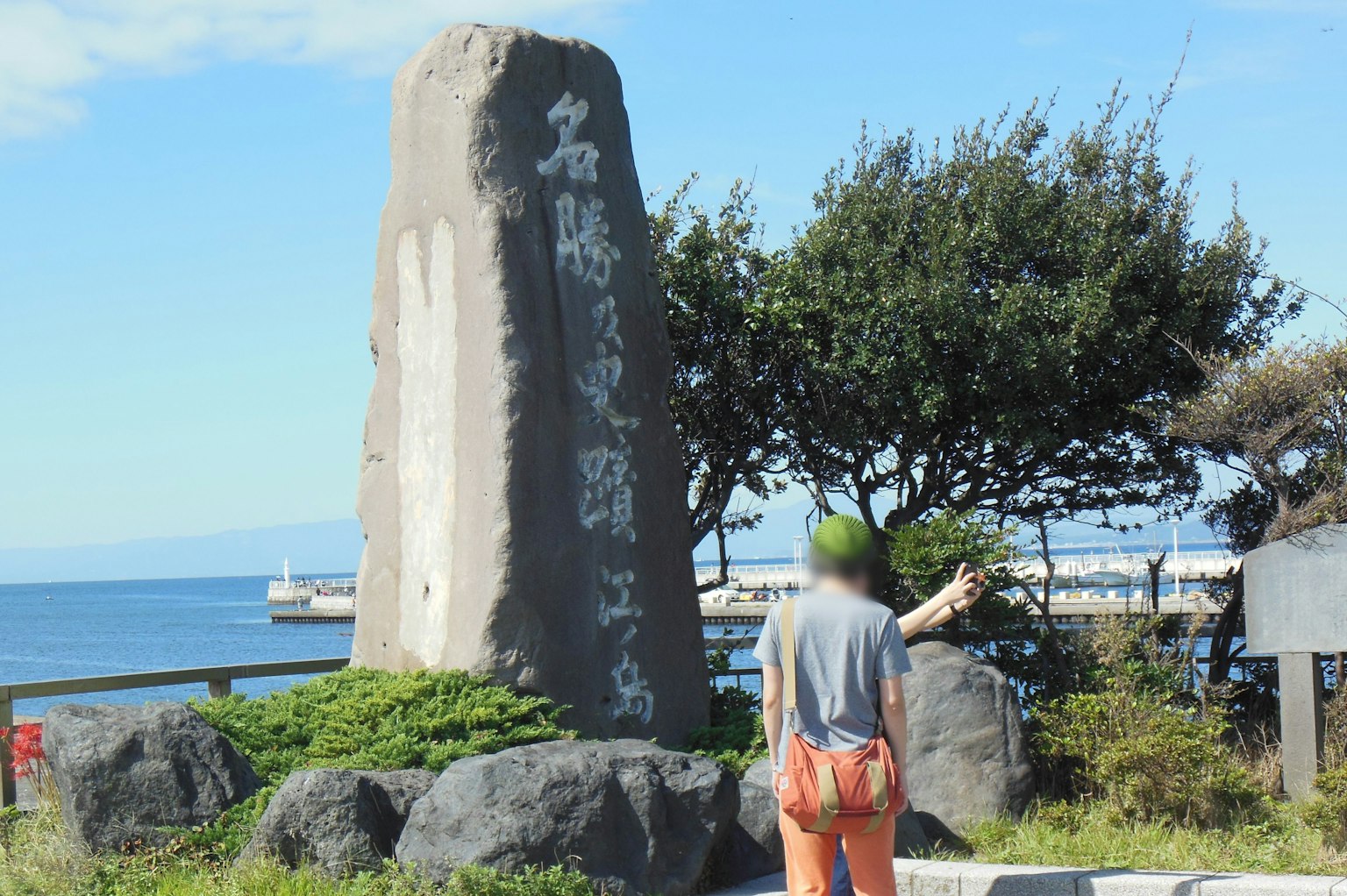 Monumen batu besar dengan tulisan di tepi laut dan seseorang di dekatnya