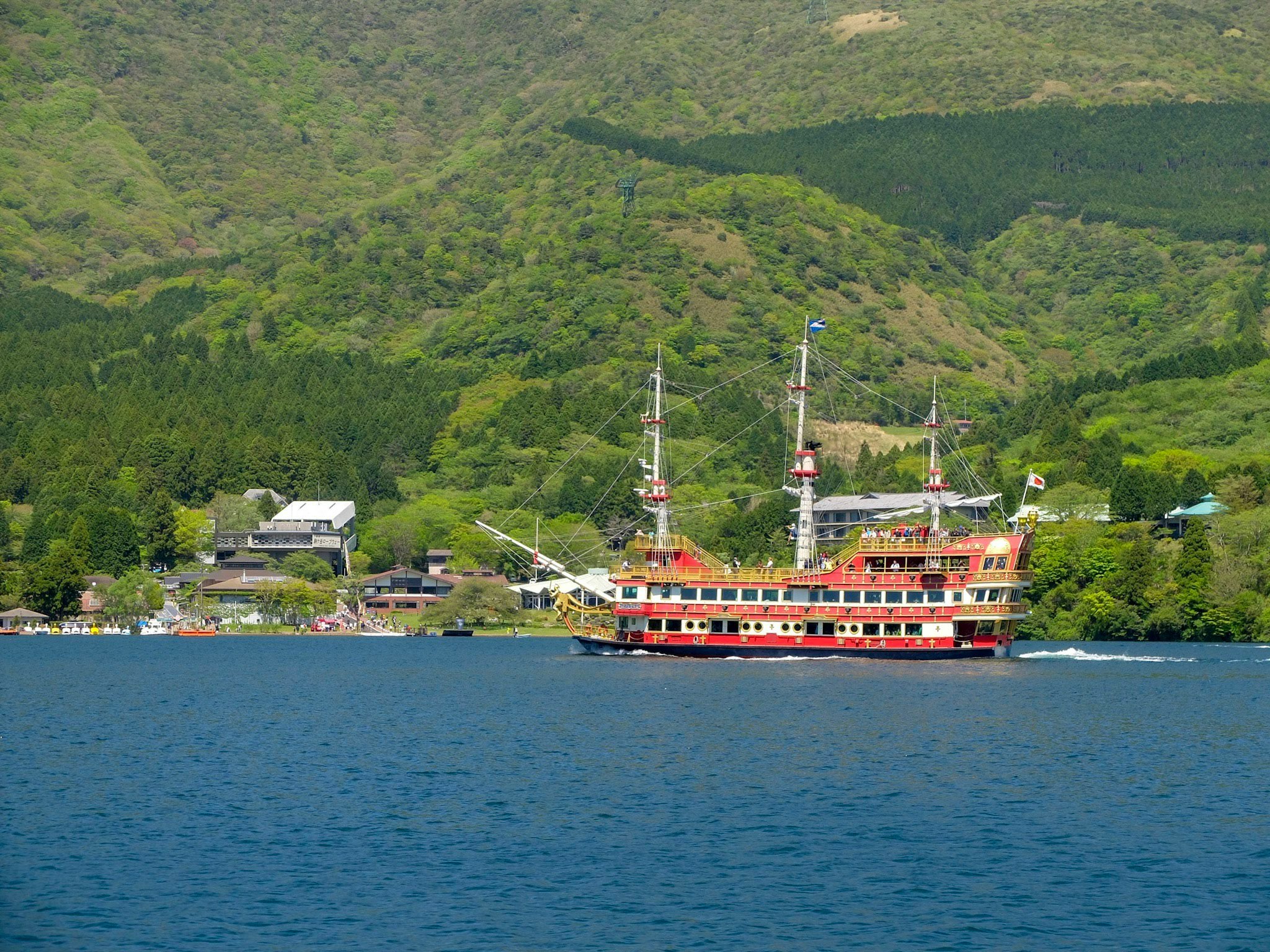 山あいの湖畔を航行する赤い観光船のある風景