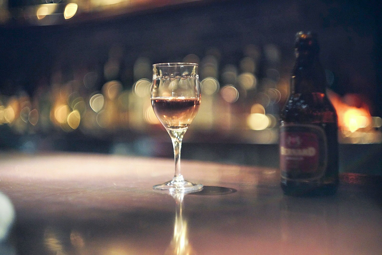 Un bicchiere di vino e una bottiglia di birra su un bancone di bar con sfondo sfocato