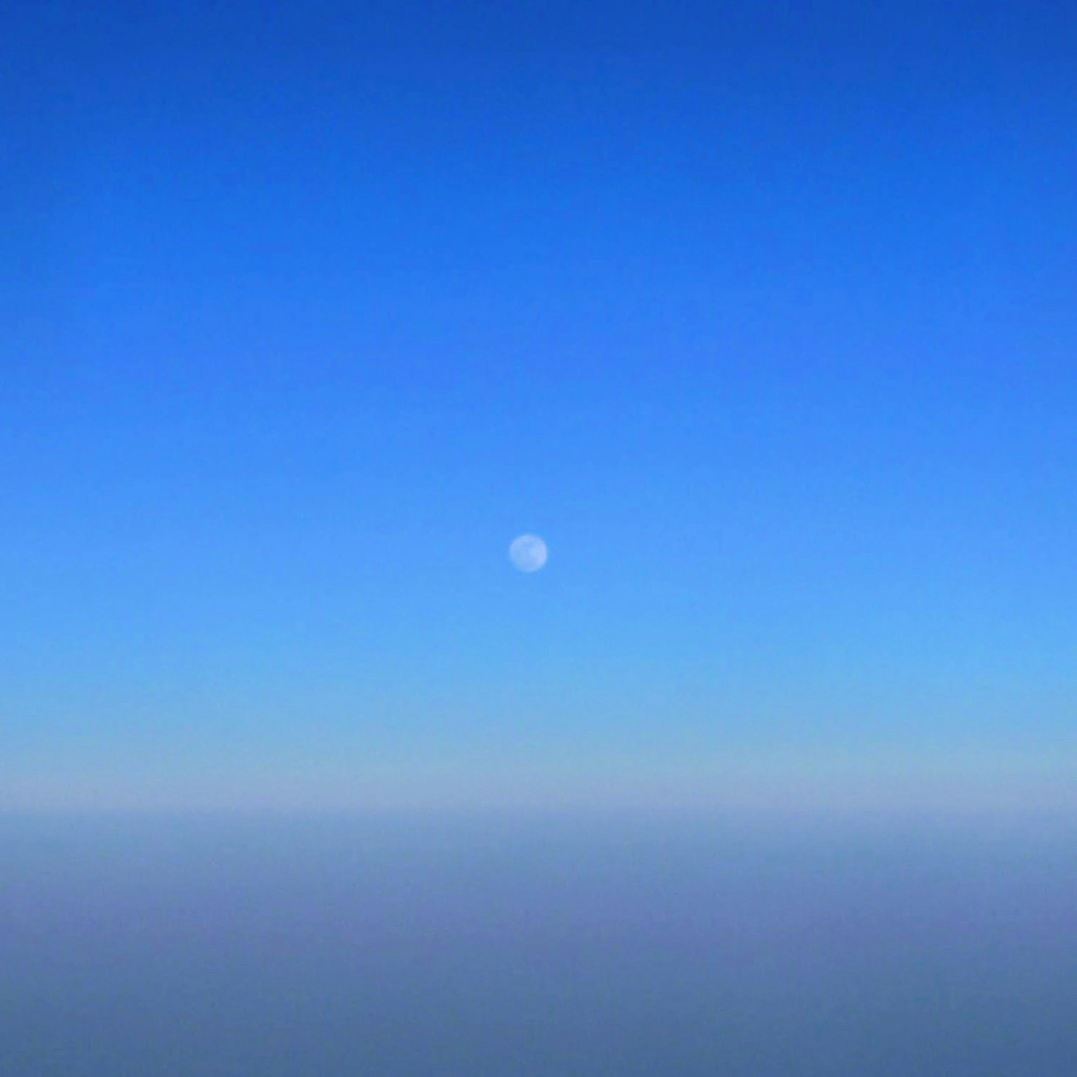 A small moon floating in a clear blue sky
