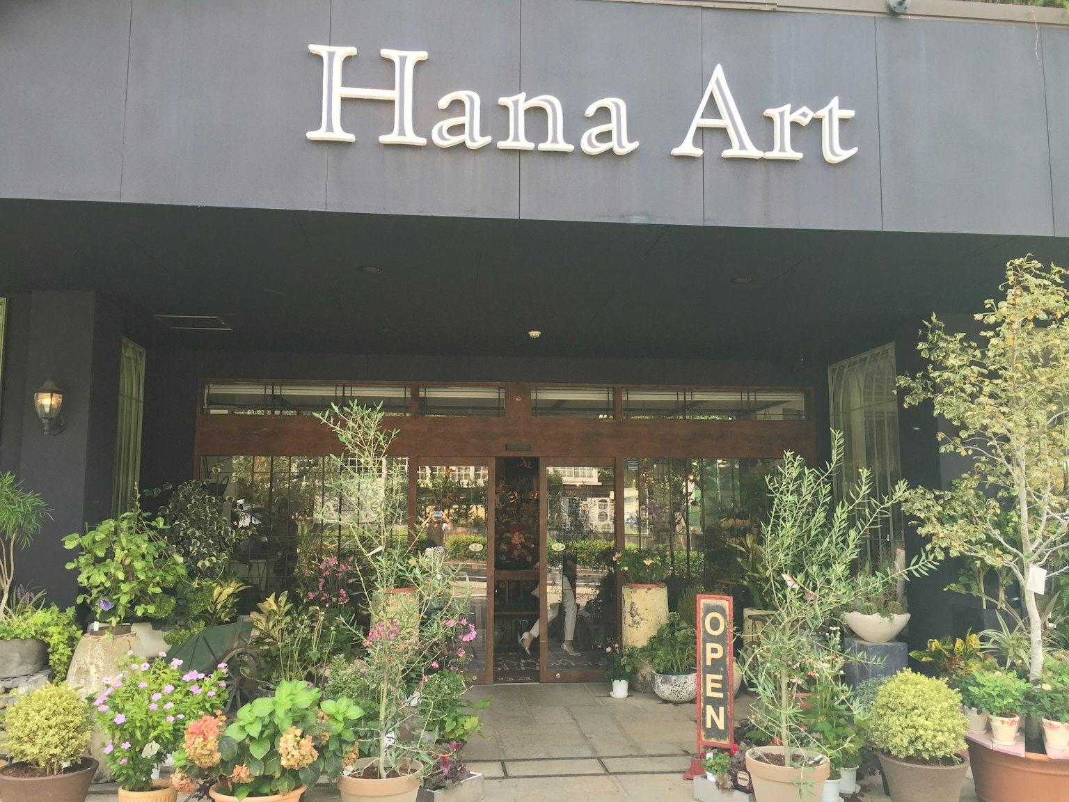 ด้านนอกของร้าน Hana Art มีต้นไม้และดอกไม้ที่อุดมสมบูรณ์ที่ทางเข้า