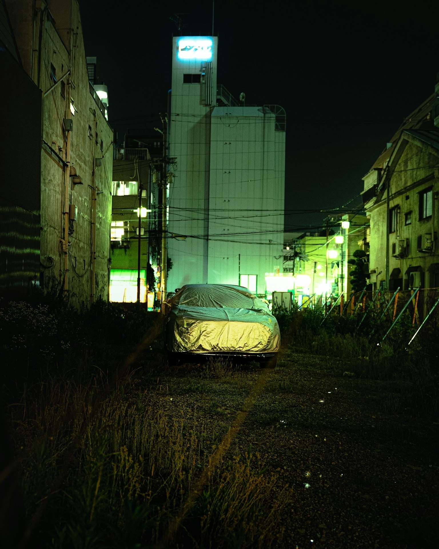 A covered car in an urban setting illuminated by green lights at night