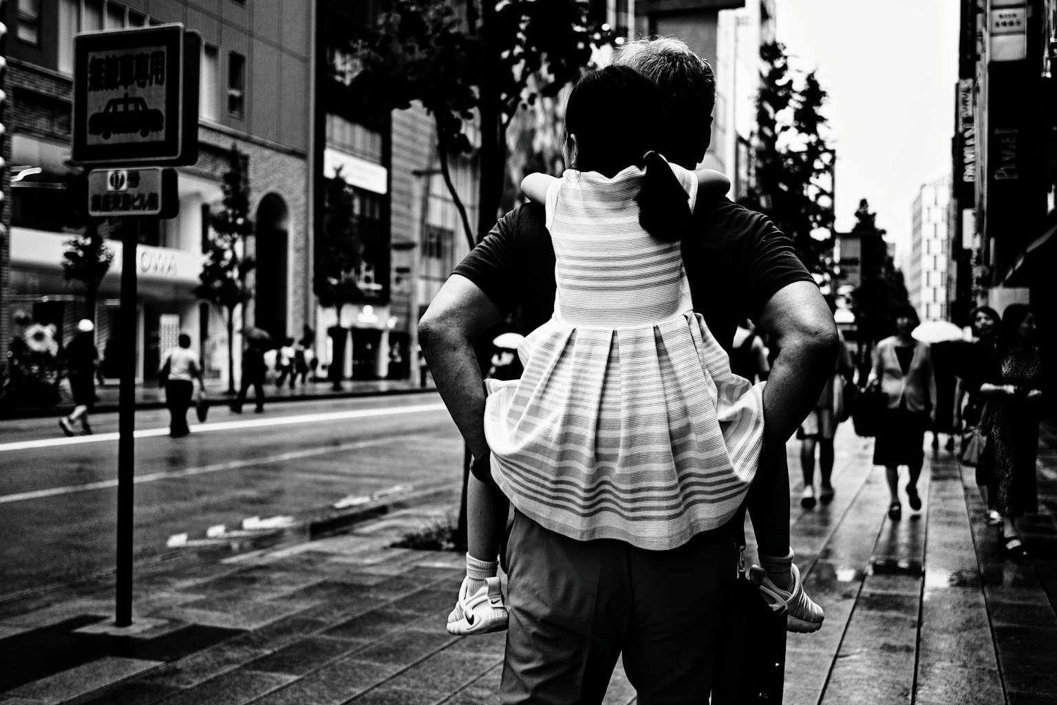 Un padre llevando a su hija en la espalda en una escena urbana en blanco y negro