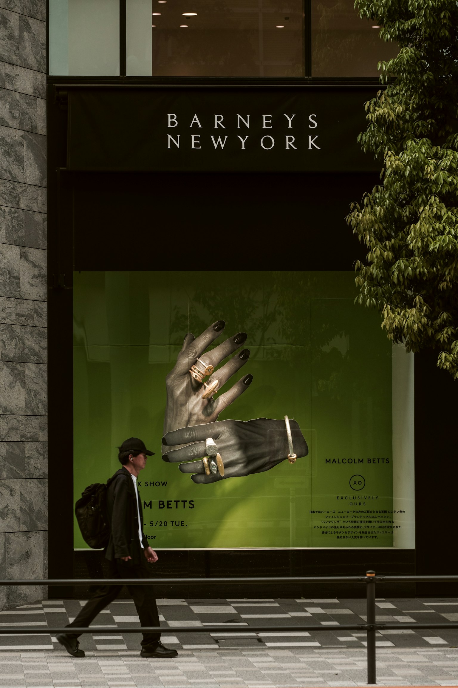 A man walking in front of Barneys New York with a green window display featuring a large hand