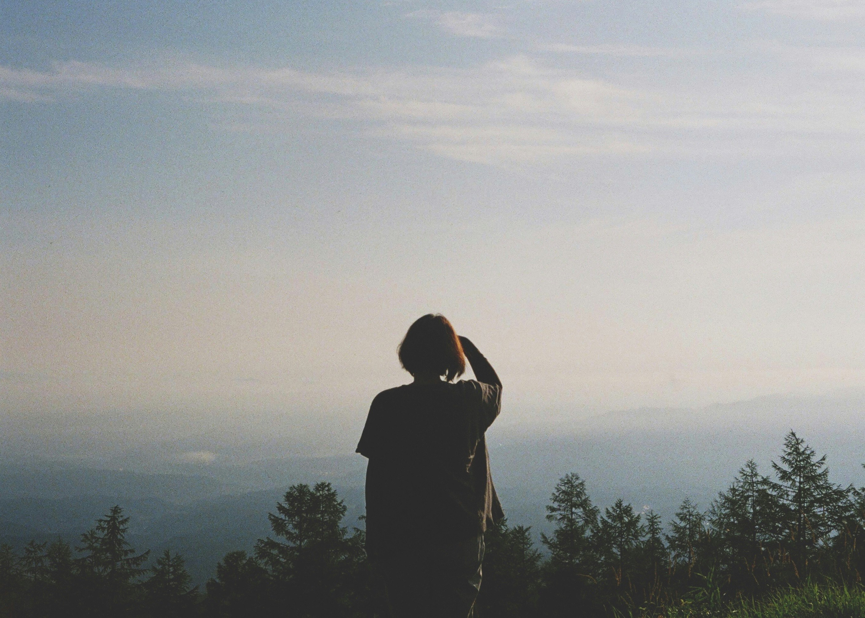 夕暮れの山並みを見つめるシルエットの人物