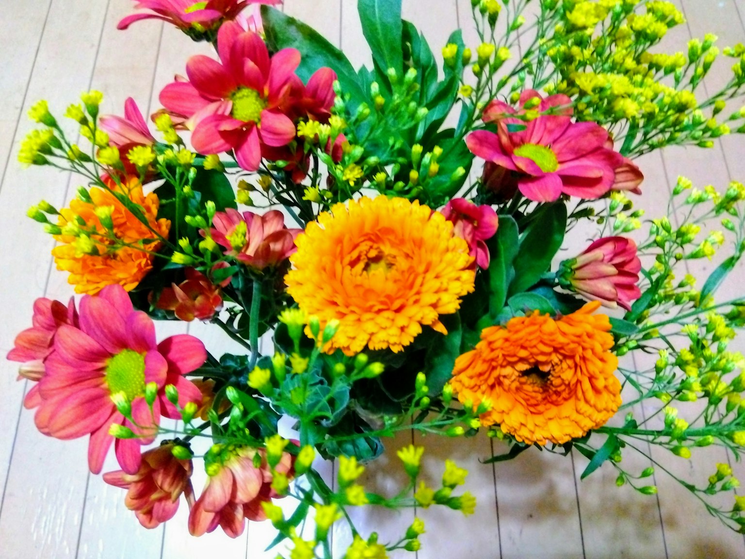 Un ramo vibrante con flores naranjas y rosas y hojas verdes