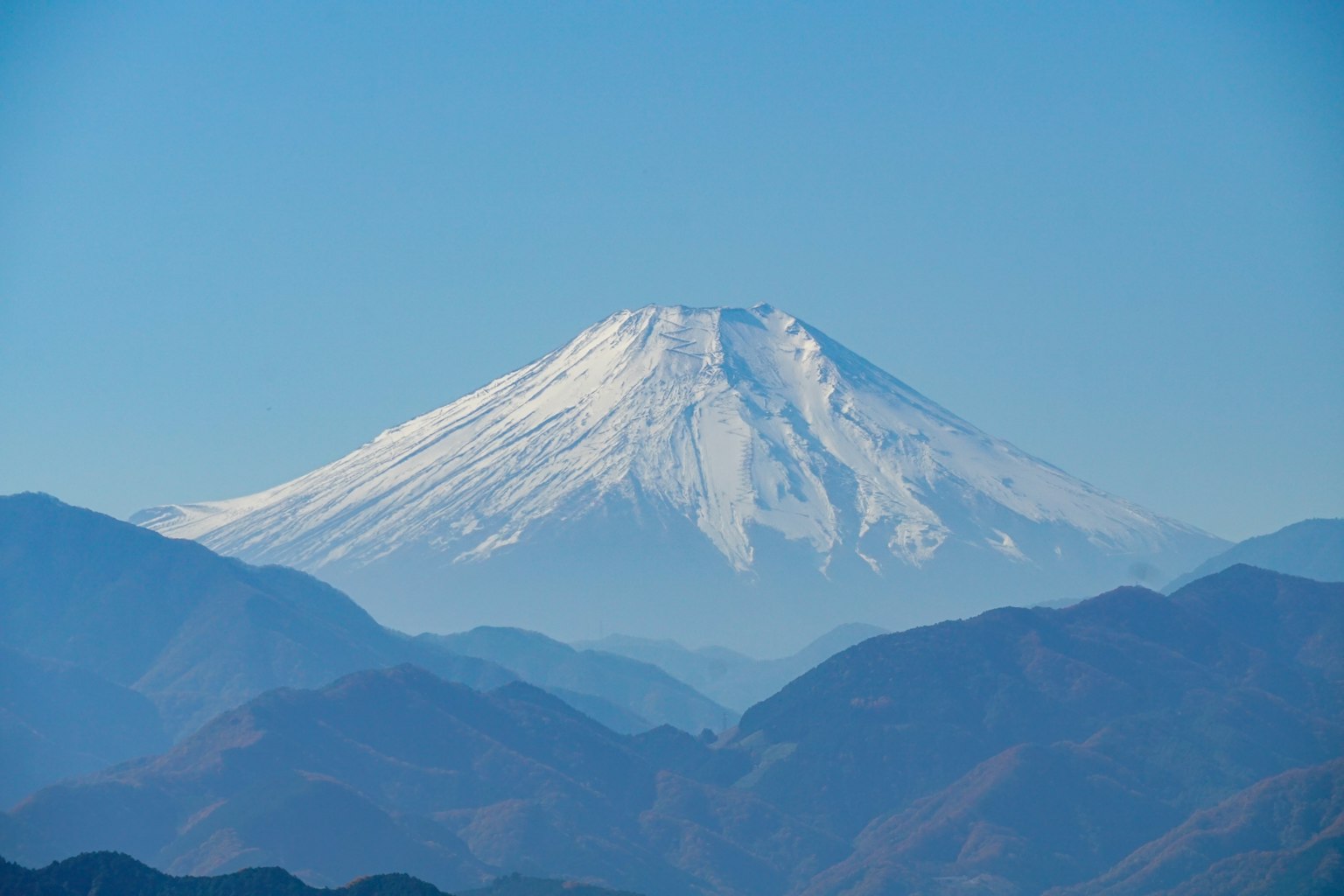 Mount Fuji's snow-covered peak stands majestically against a clear blue sky and surrounding mountains
