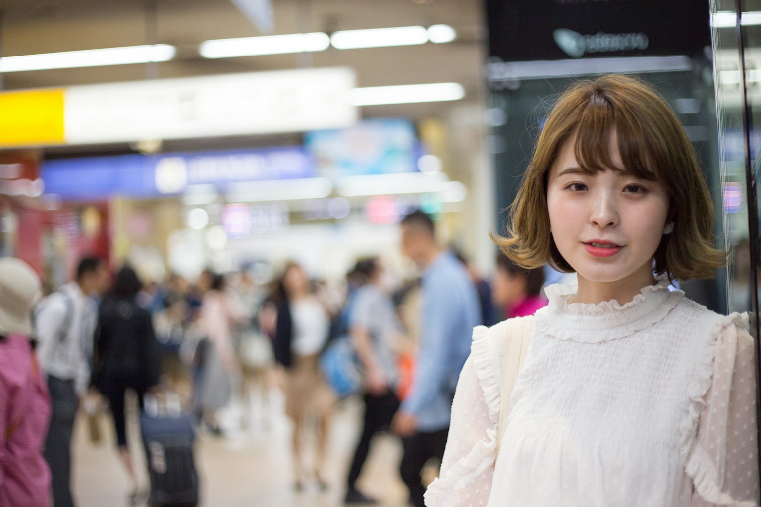 Potret wanita tersenyum di stasiun dengan latar belakang orang-orang yang kabur