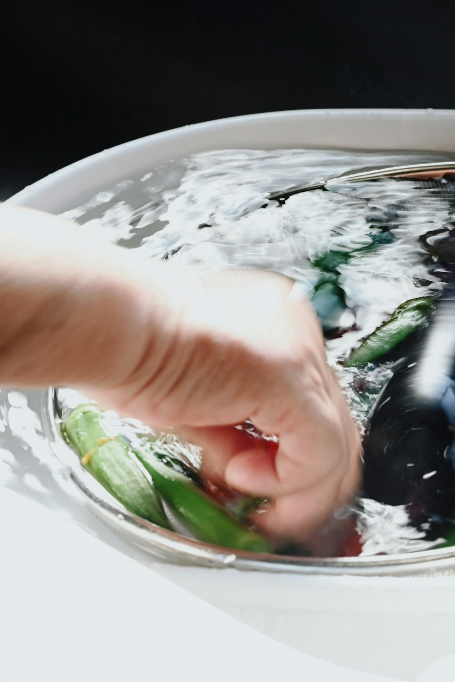 Mano che lava verdure in una ciotola d'acqua