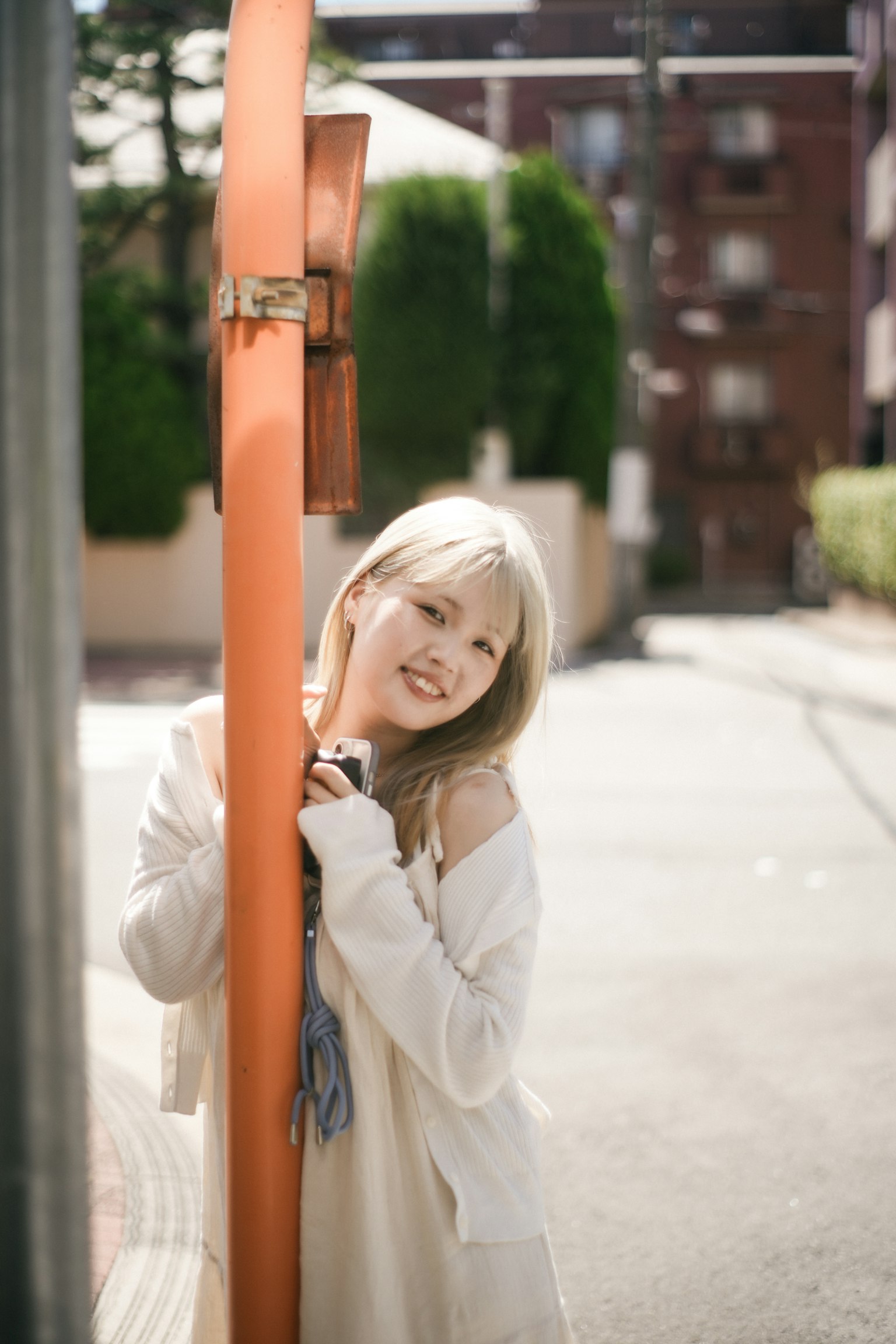 젊은 여성이 주황색 기둥에 기대어 미소 짓고 있다