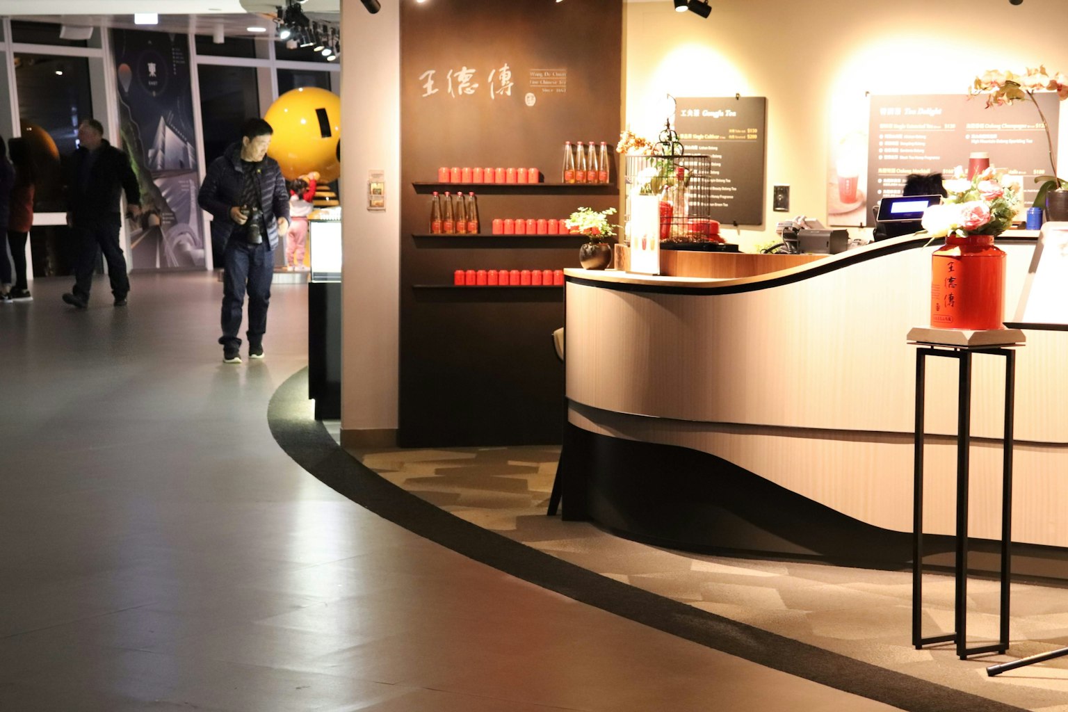 现代接待区，柜台上展示红色物品，背景有人在走动