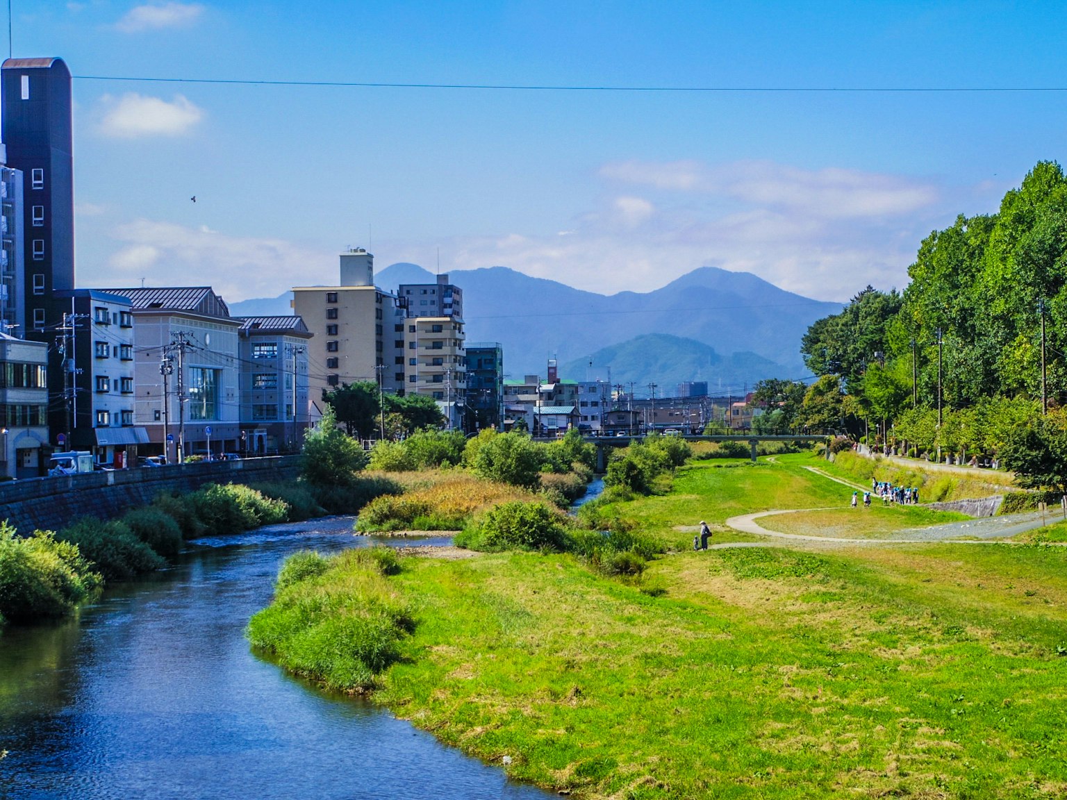 A scenic view featuring a river under a blue sky with lush greenery and distant mountains