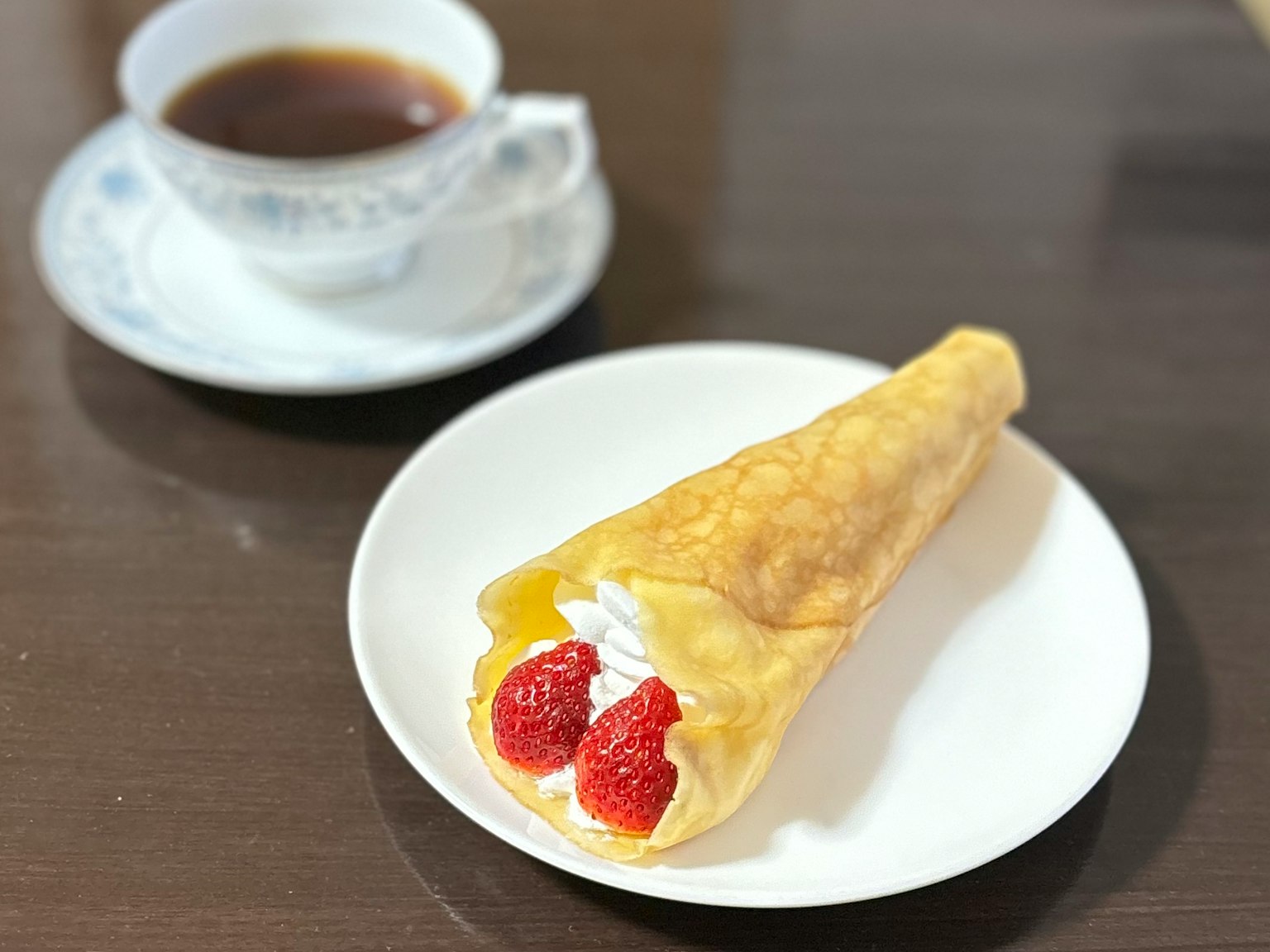 Dessert crepe filled with strawberries and whipped cream next to a cup of coffee