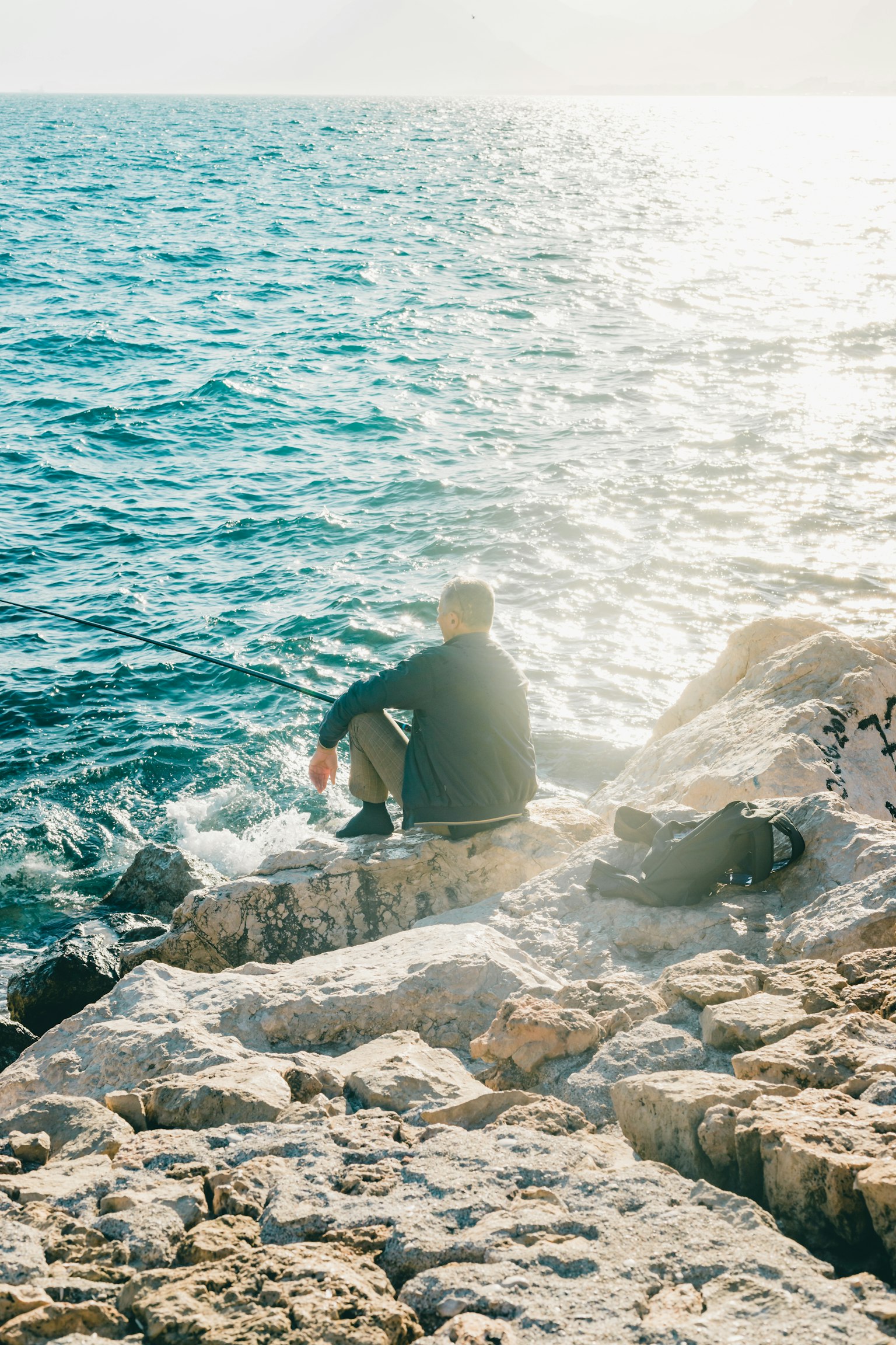 Hombre sentado en rocas junto al mar con agua brillante