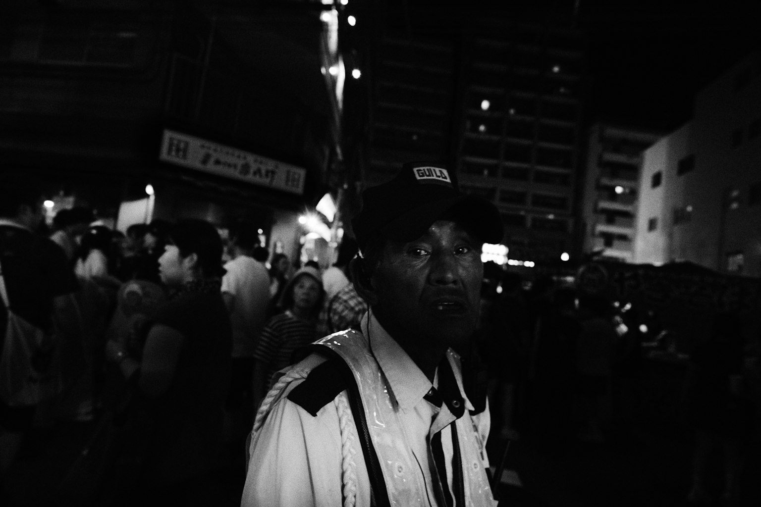 A security guard stands in a crowded street at night with people around