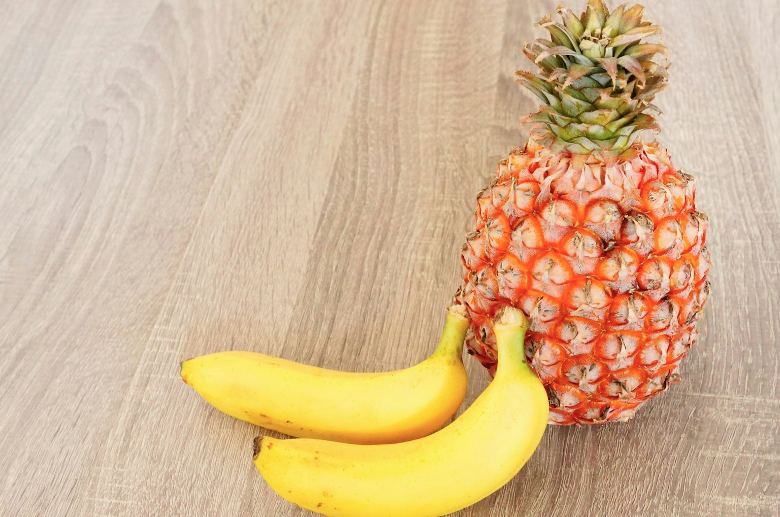 Combinación de piña y plátanos sobre una mesa de madera