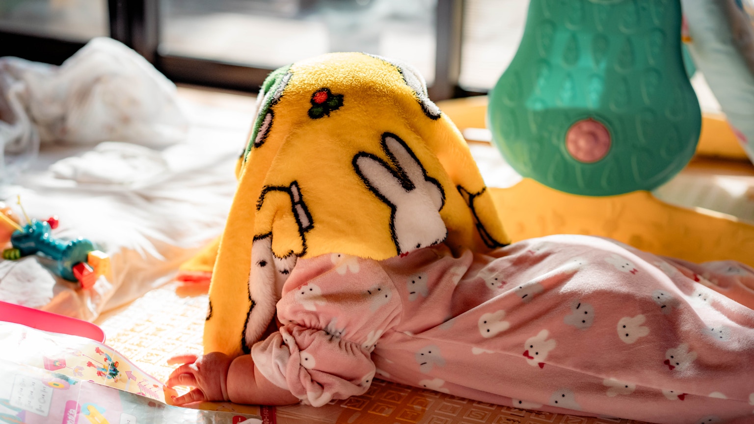A baby lying on the floor covered with a yellow rabbit blanket in a cozy indoor setting