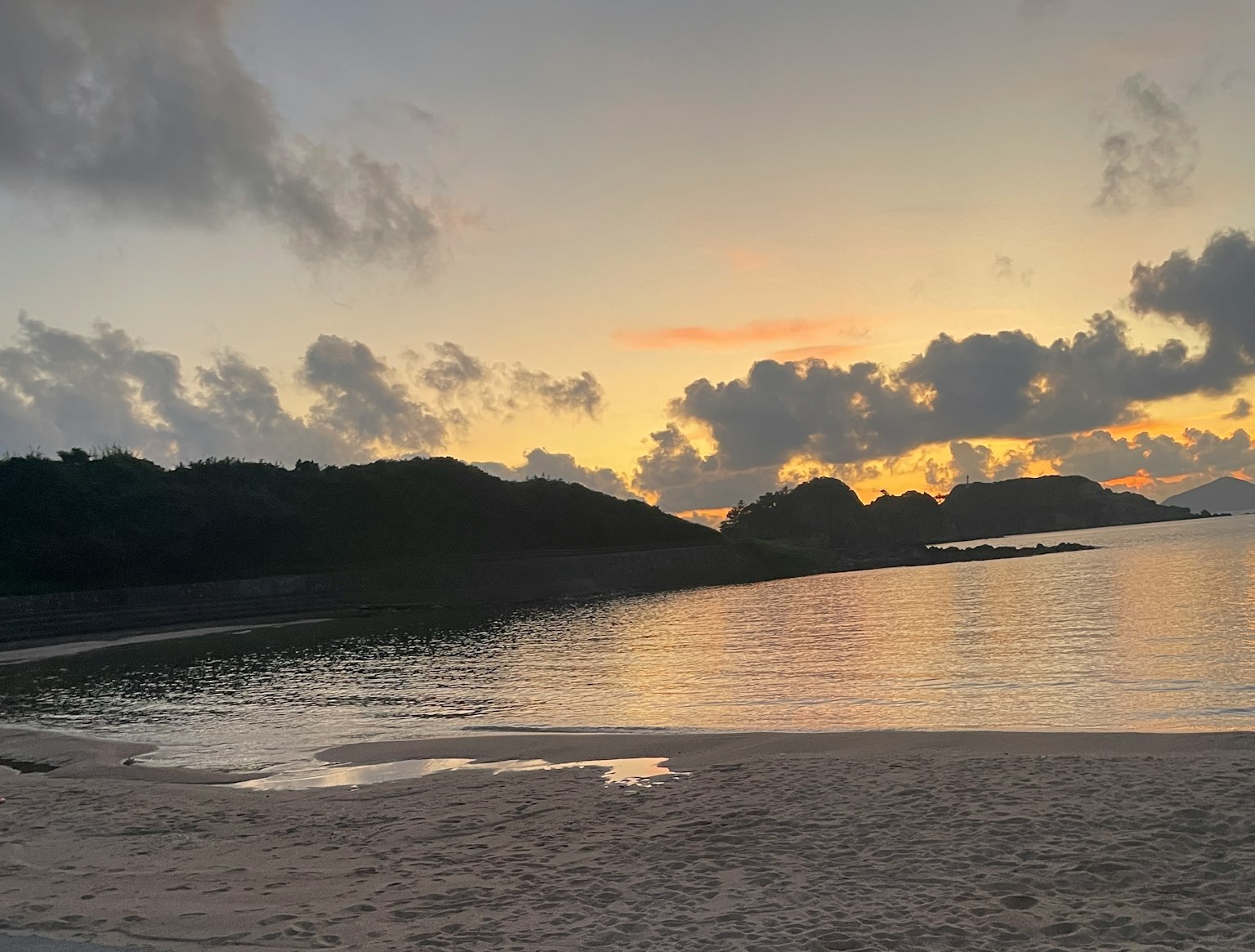 Scenic beach view at sunset with calm waters and hills in the background