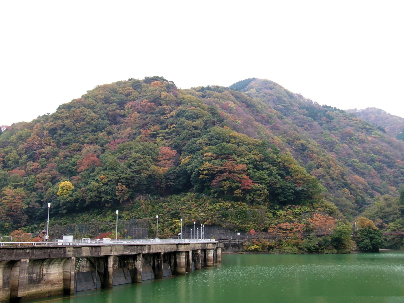 Malersicher Blick auf einen Pier mit grünem Wasser und buntem Herbstlaub auf den Hügeln