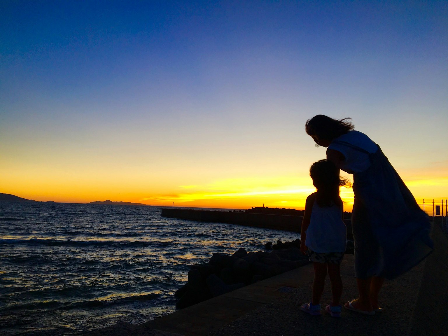 海岸上夕陽下的父母與孩子剪影
