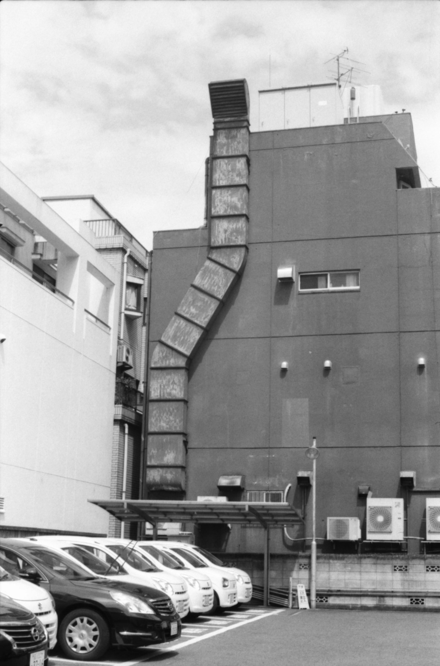 Black and white image of a building with a curved exhaust duct and parked cars