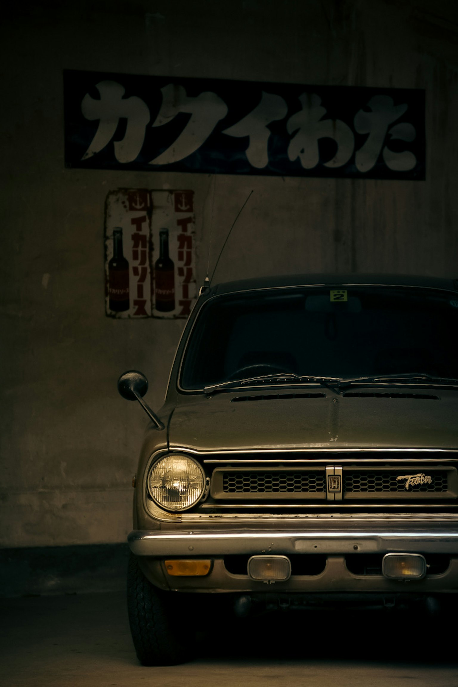 古い車が暗いガレージに停まっている背景には日本語の看板がある