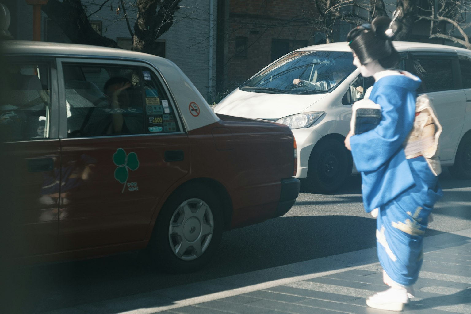 Una mujer con kimono azul de pie frente a un taxi