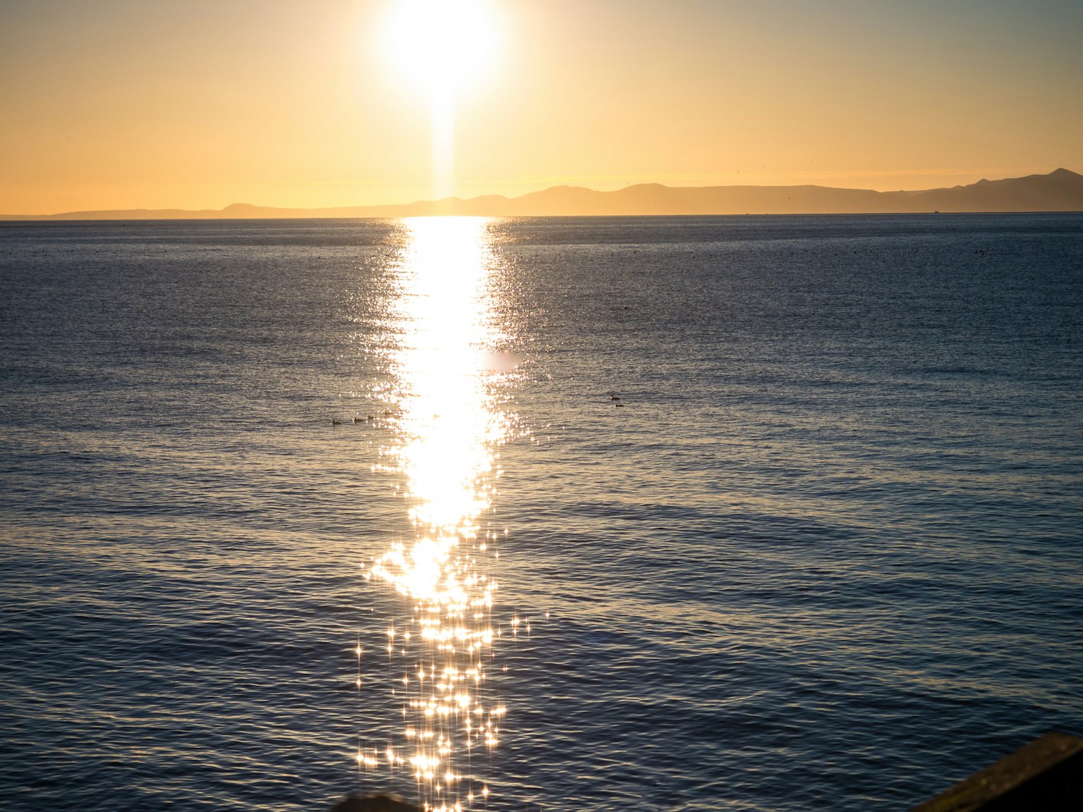 พระอาทิตย์ตกเหนือคลื่นมหาสมุทรที่สงบพร้อมกับการสะท้อนแสง