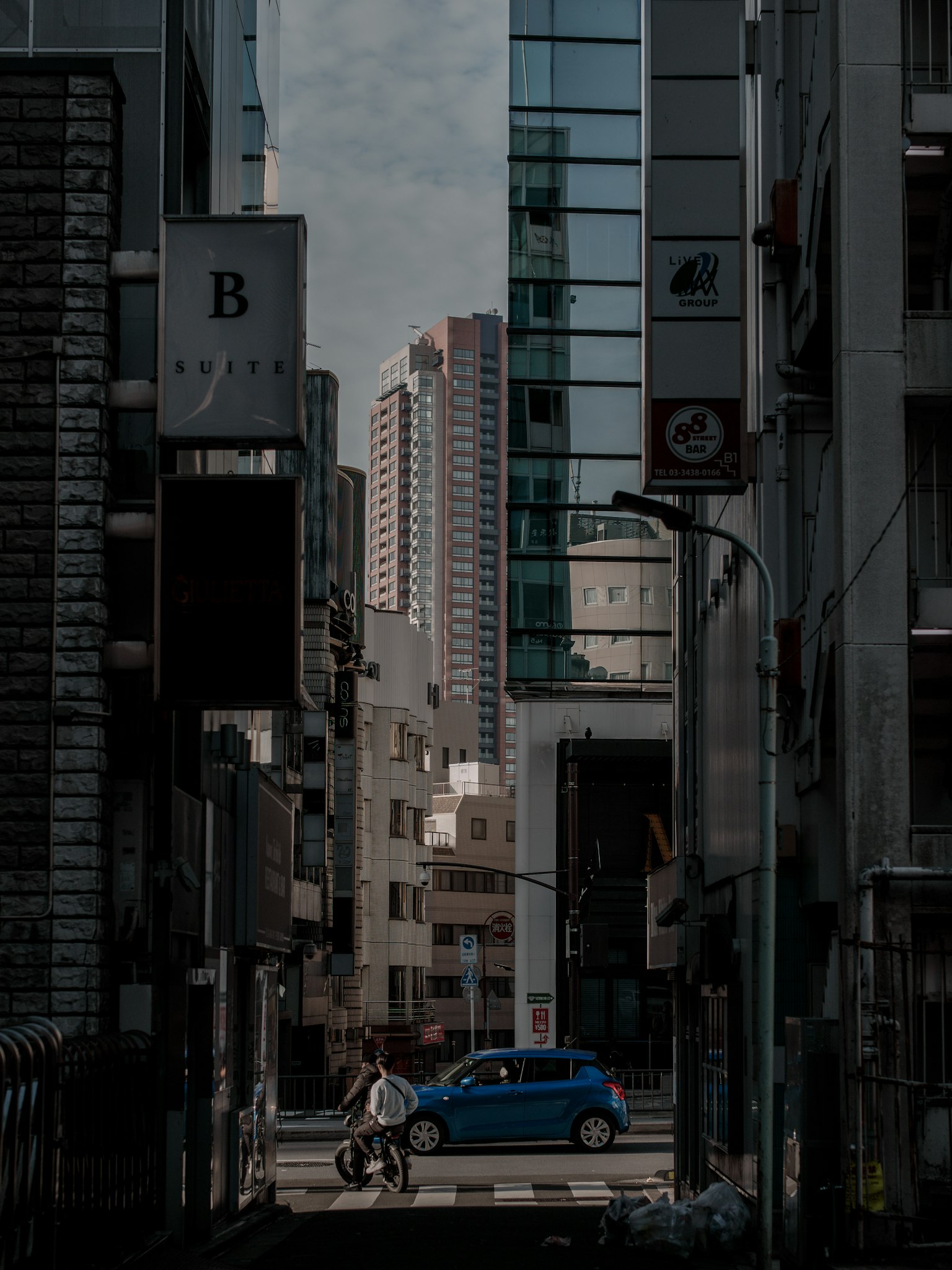 狭窄街道场景，背景是高楼和一辆蓝色汽车