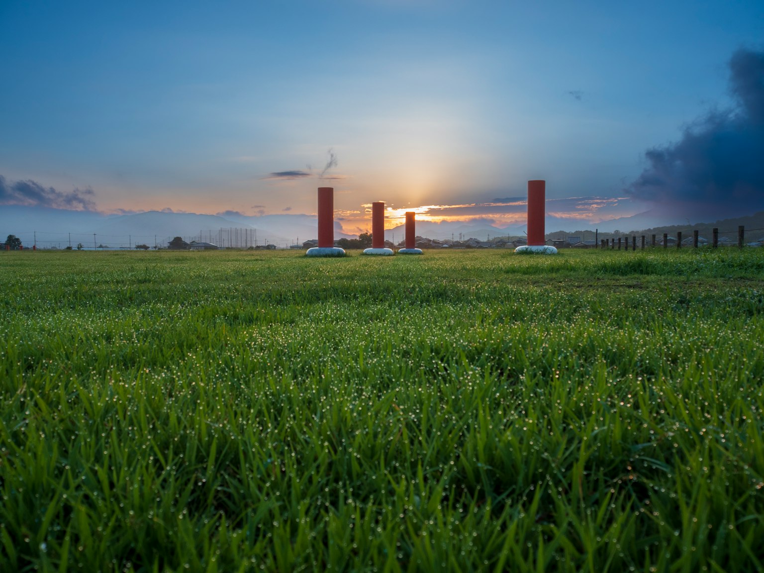 Green grass field with red pillars at sunset