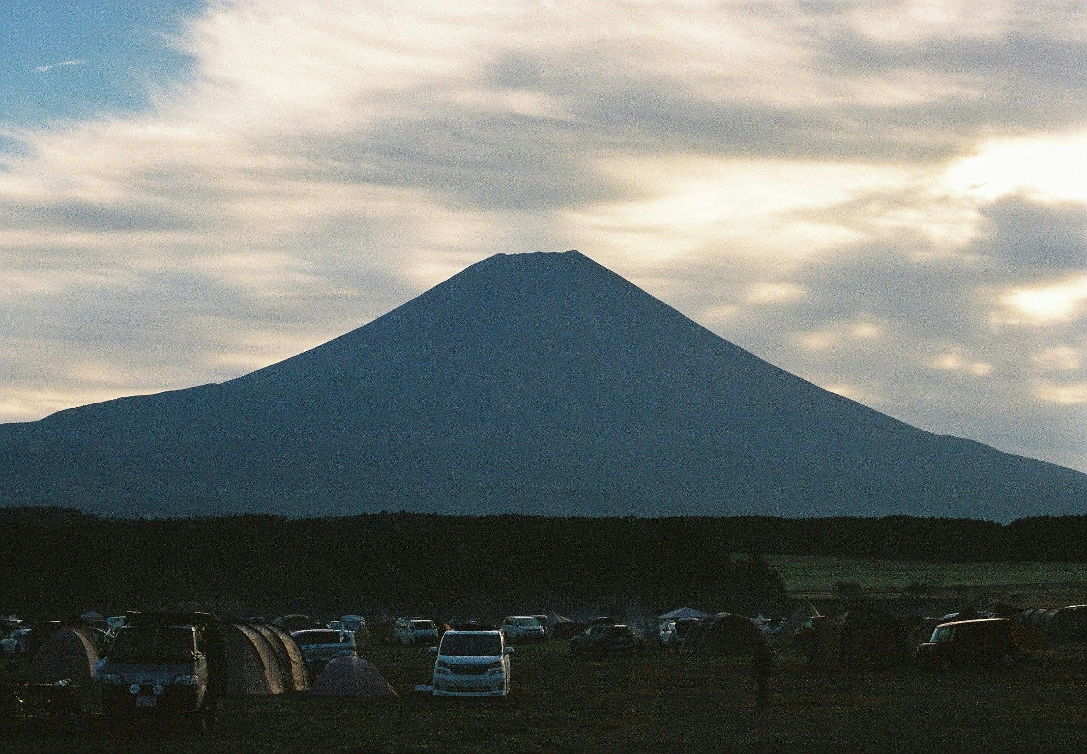 夕暮れの草原にそびえる円錐形の山と駐車場の車