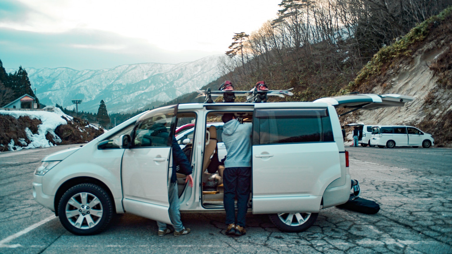 Two individuals organizing luggage next to a white van in a mountainous landscape