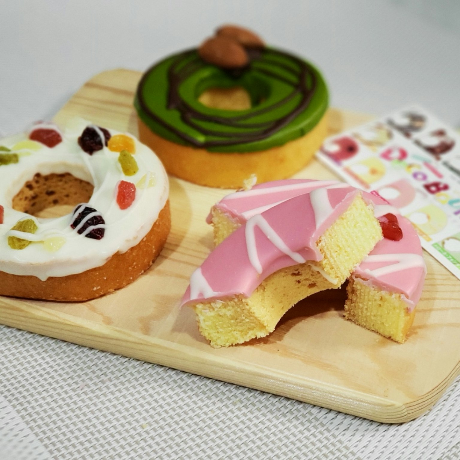 Ciambelle colorate disposte su un piatto di legno con una ciambella rosa parzialmente morsa