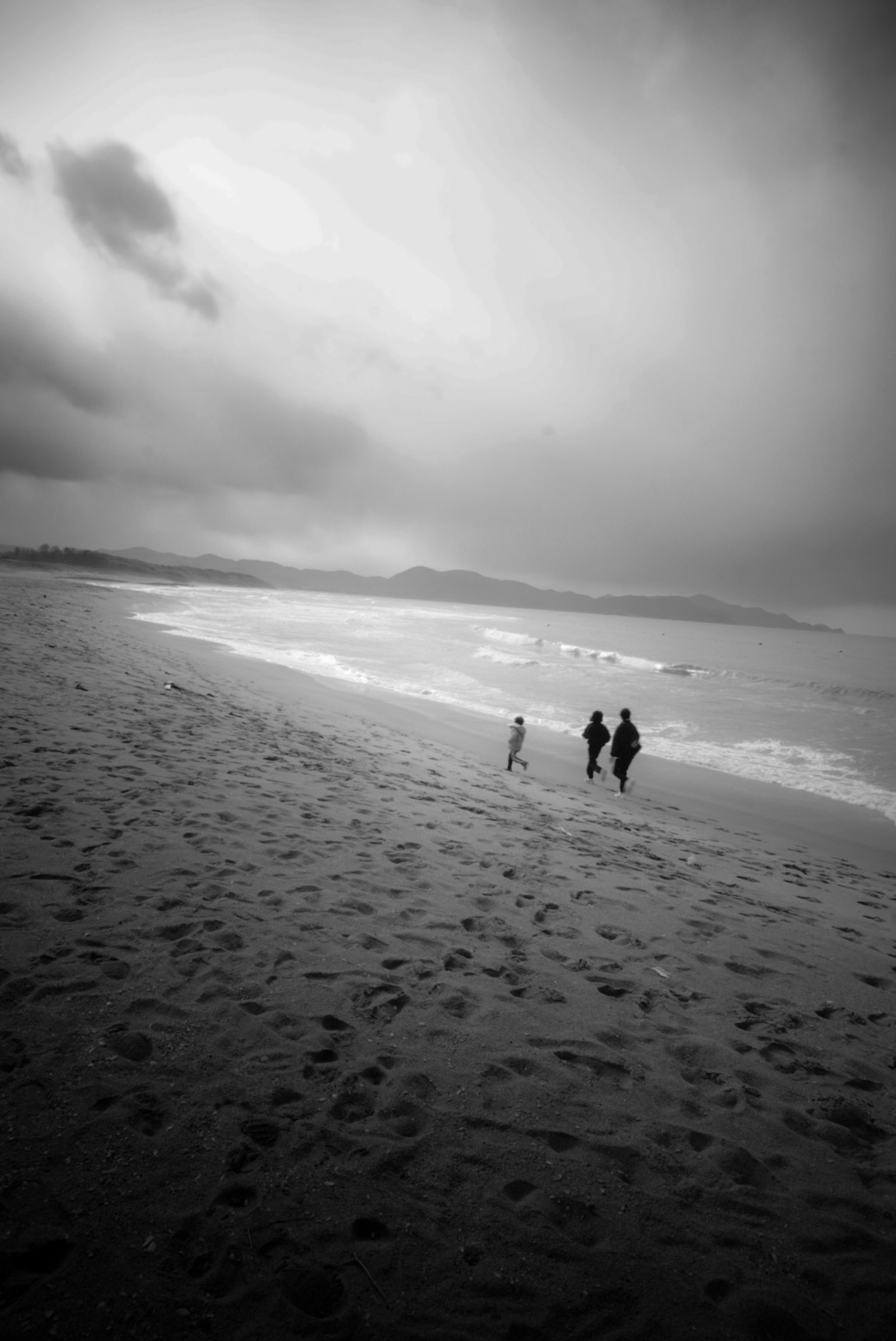 เงาของผู้คนเดินบนชายหาดขาวดำพร้อมกับคลื่น