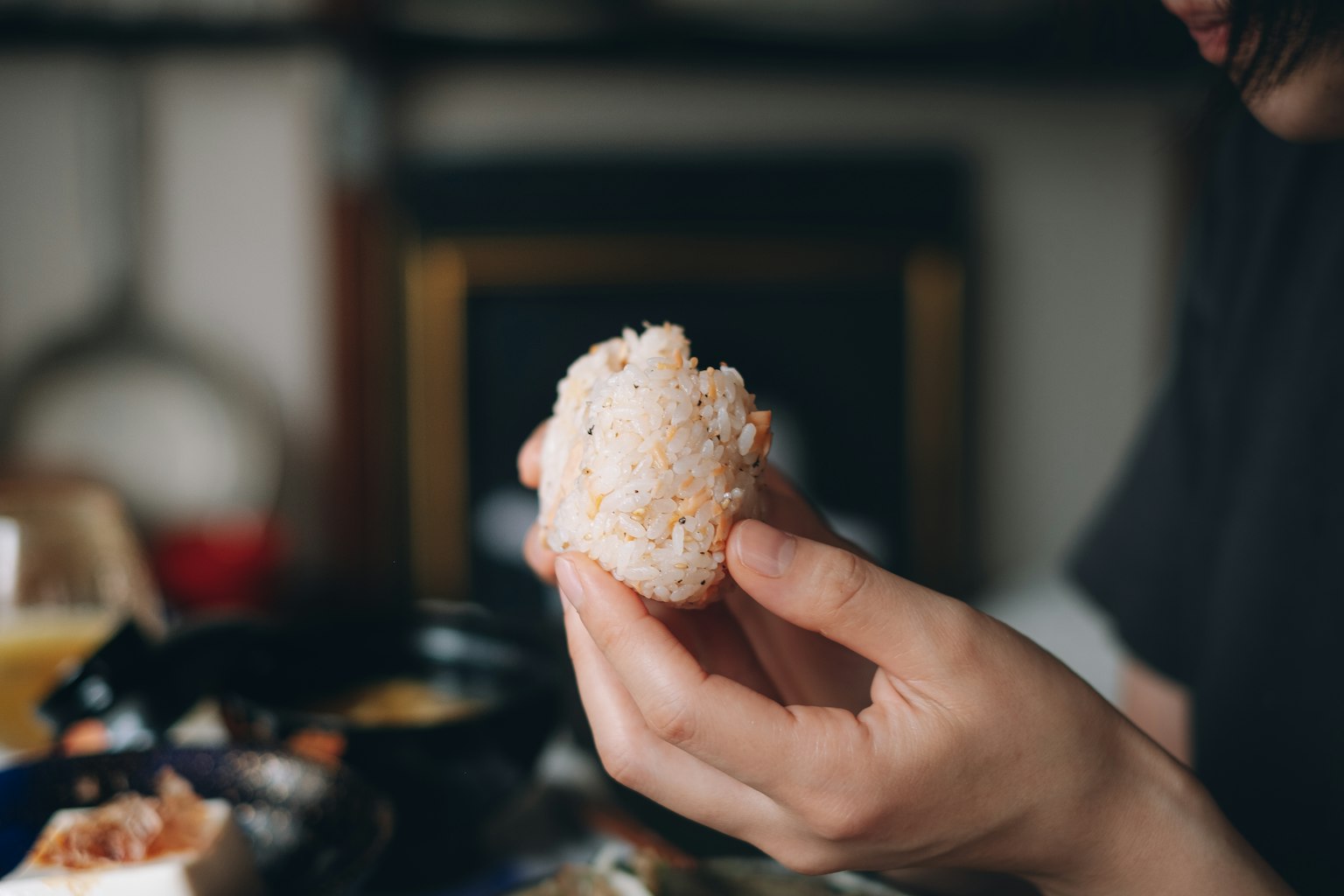 Une main tenant un onigiri avec divers plats en arrière-plan