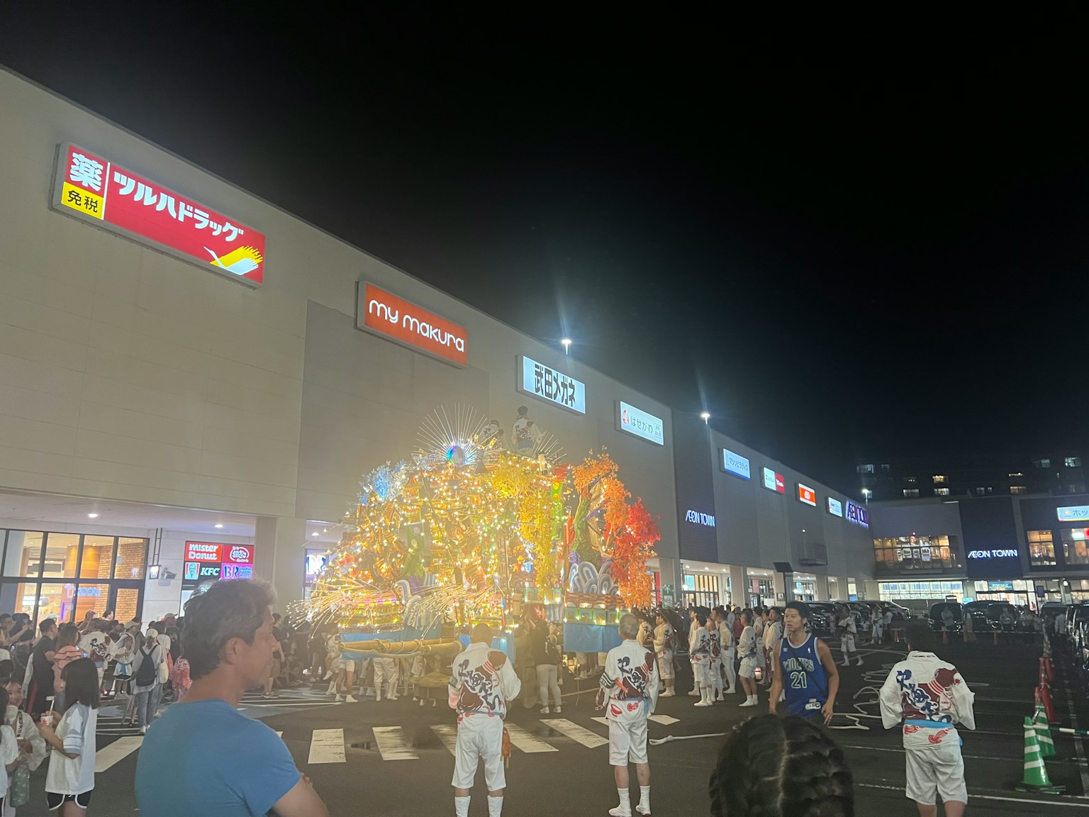 夜の祭りの様子で、色とりどりの山車が展示されている人々が集まっている