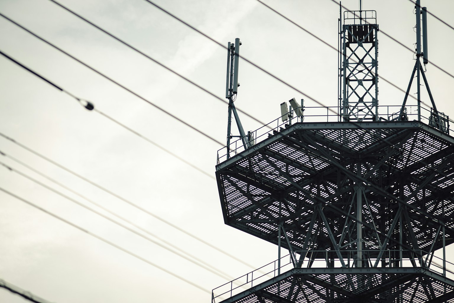 Primer plano de una torre de transmisión con líneas eléctricas bajo un cielo nublado