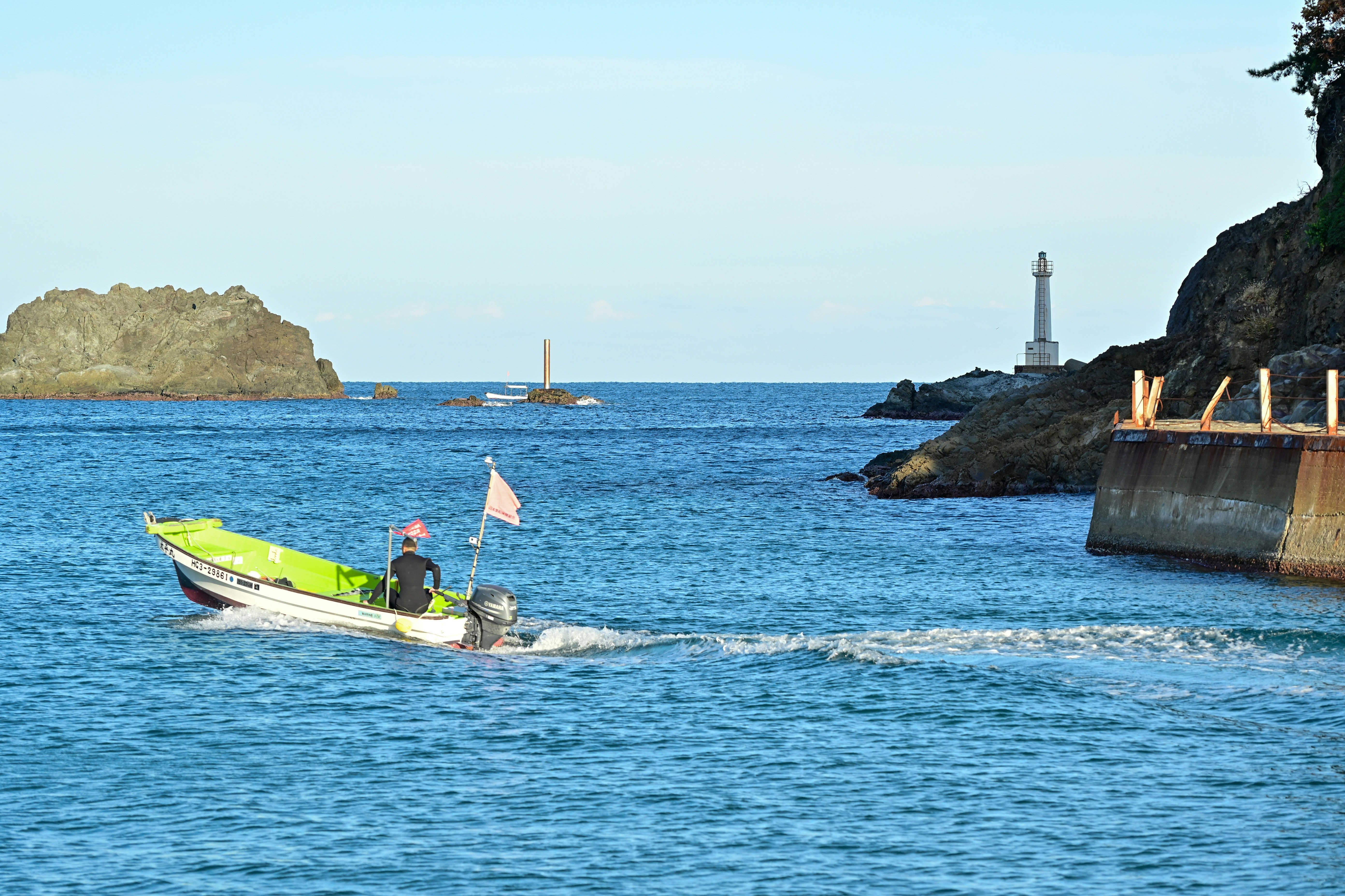海上を進む小型ボートと灯台のある海岸の景色