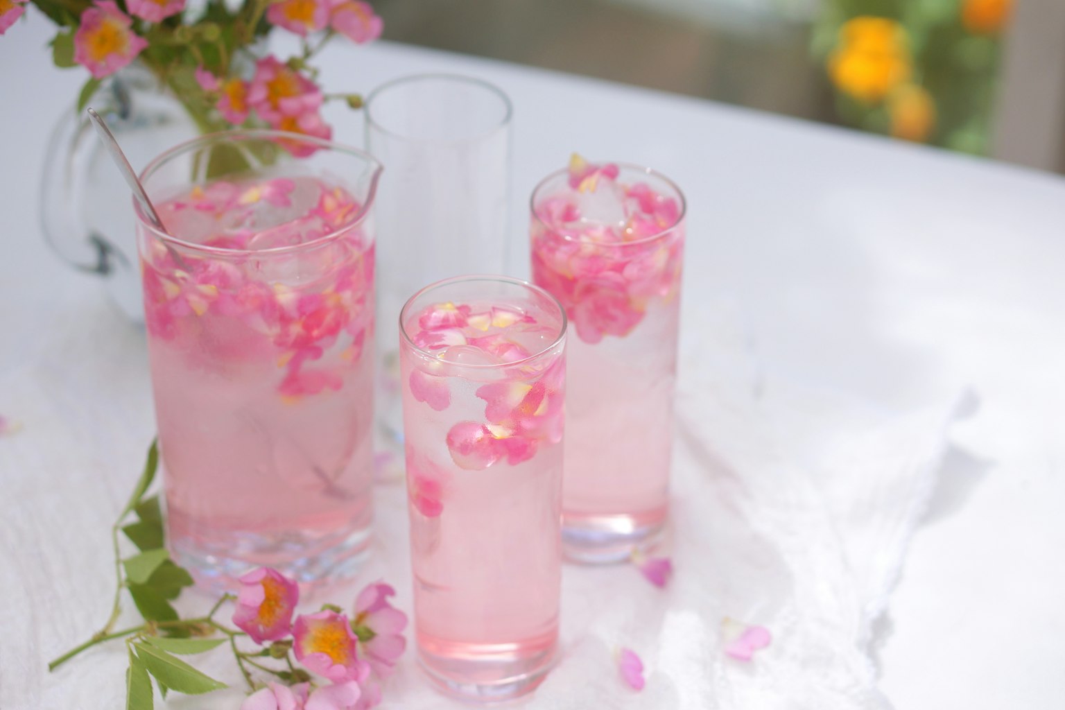 Trois verres de boisson rose avec des pétales de fleurs sur une table blanche