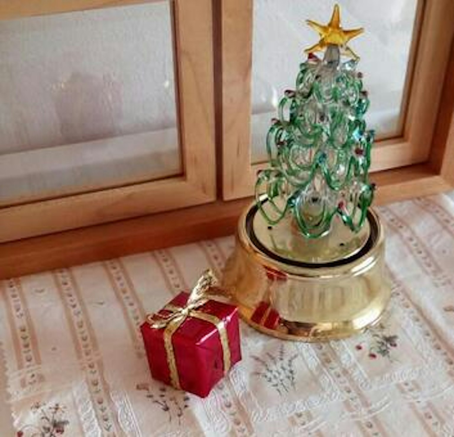 Albero di Natale in vetro verde con base dorata e una scatola regalo rossa su un tavolo decorato