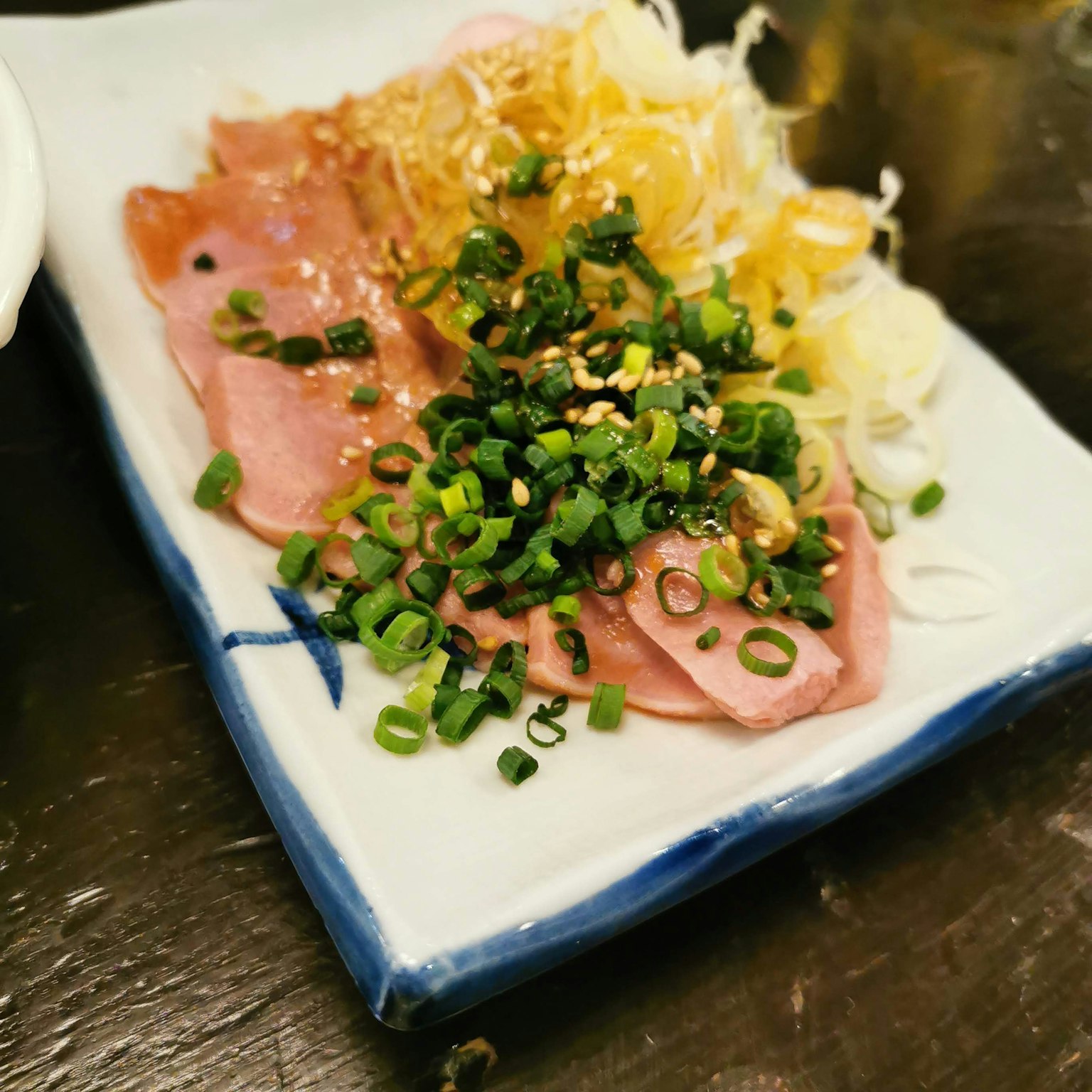 一小盤切片火腿，上面撒有切碎的蔥和芝麻