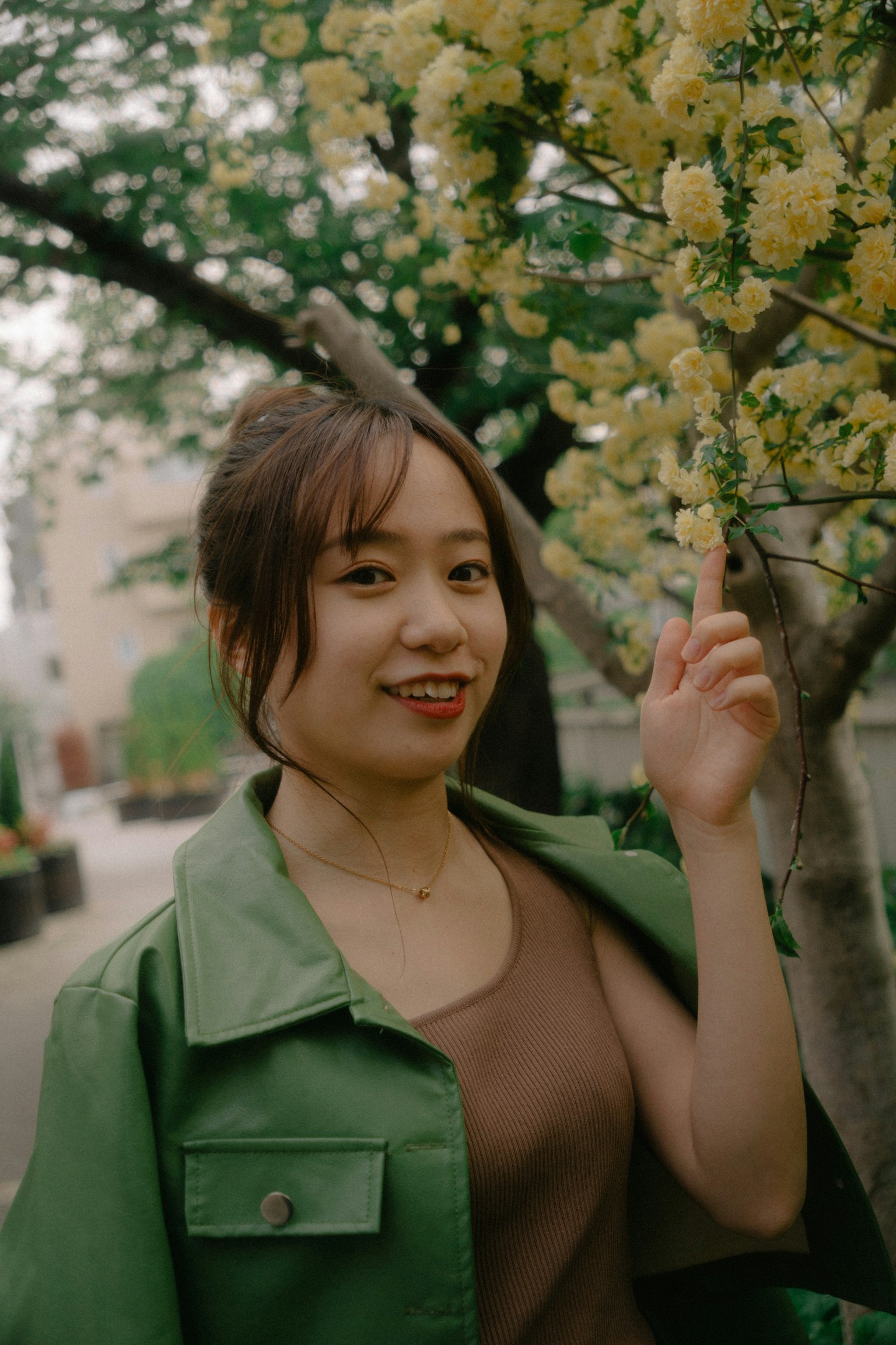 A woman in a green jacket pointing at flowers in a park setting