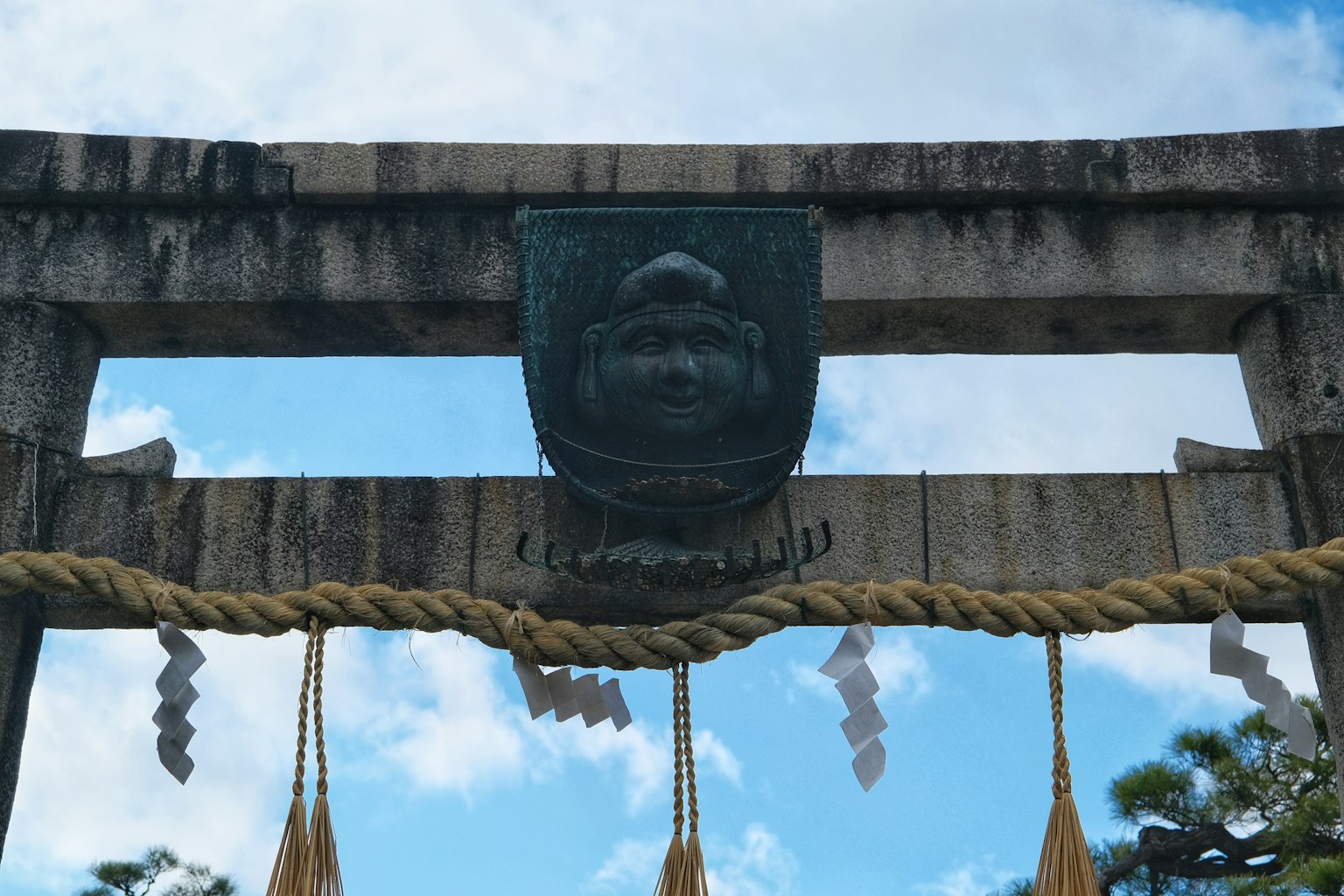 Torii mit einer Göttergesichtsskulptur vor blauem Himmel