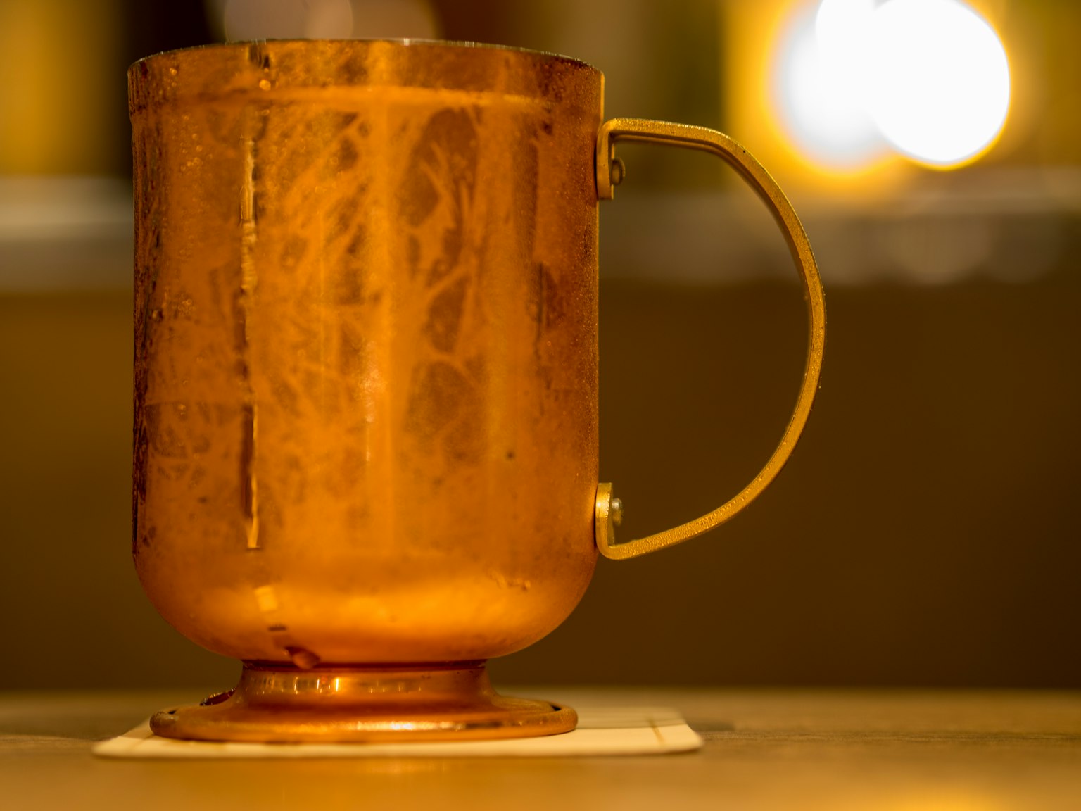 Una tazza di rame con una finitura dorata su un tavolo con luci sfocate sullo sfondo