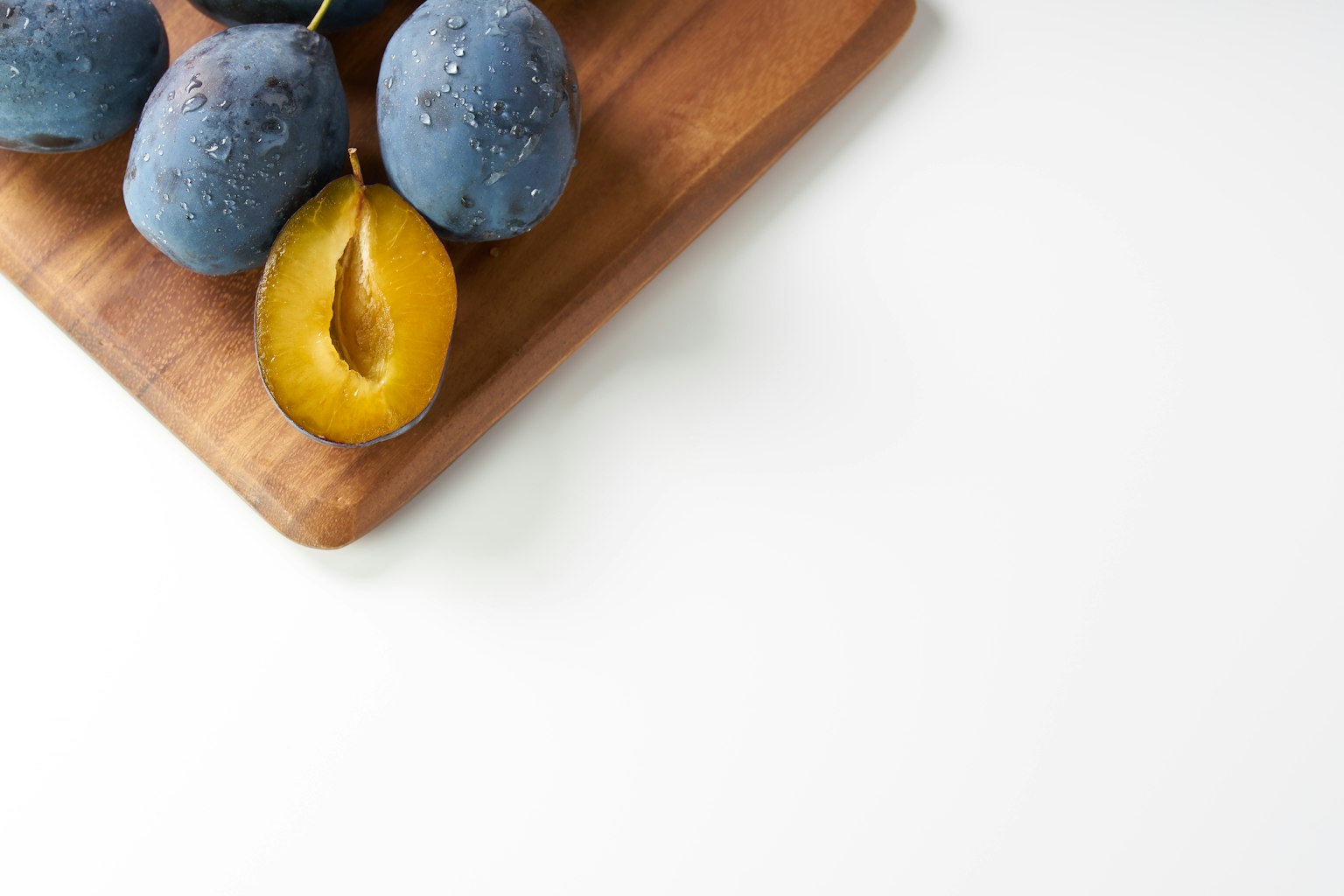 Prunes bleues et une prune jaune tranchée sur une planche en bois