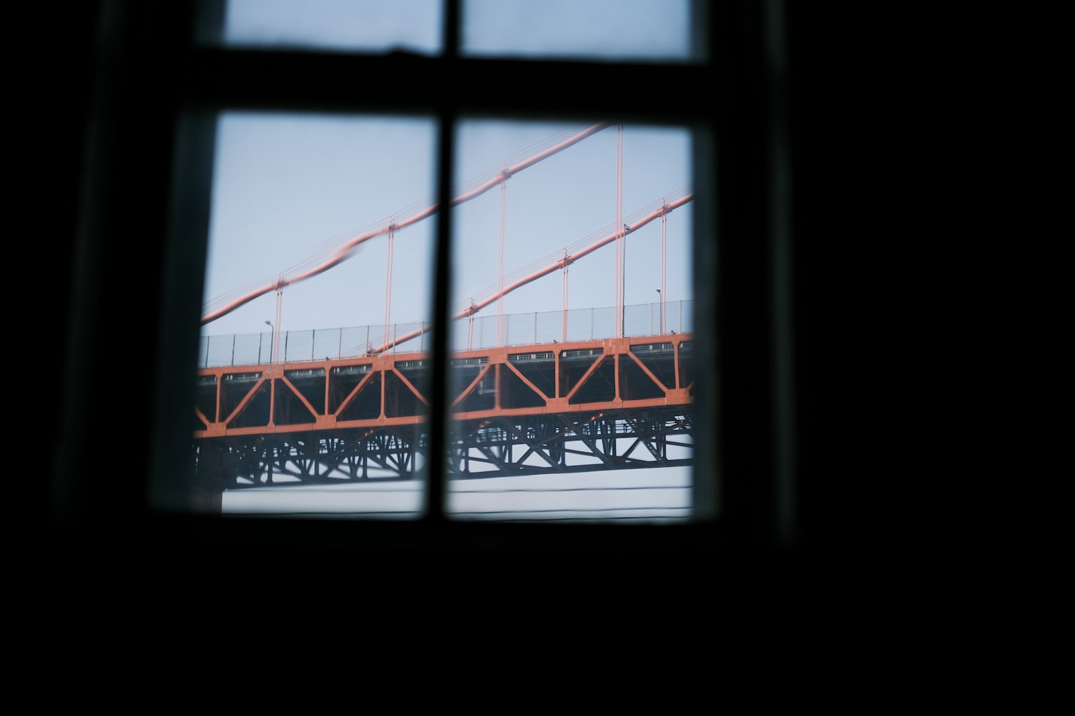 Vista de un puente naranja a través de una ventana con cielo nublado