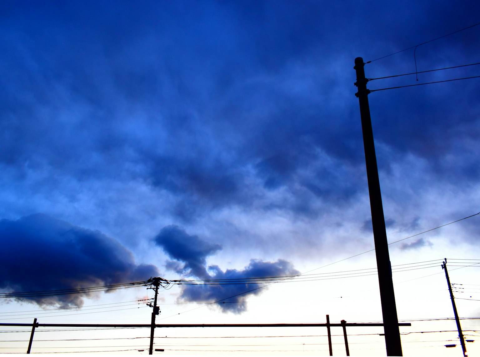 Landschaft mit blauem Himmel und dunklen Wolken sichtbarer Strommast und Stromleitungen