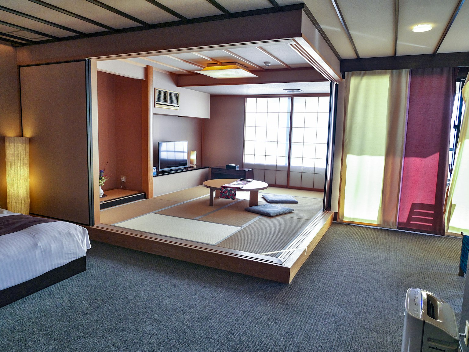 Habitación espaciosa de estilo japonés moderno Área de estar con tatami y televisión Luz natural que entra por grandes ventanas