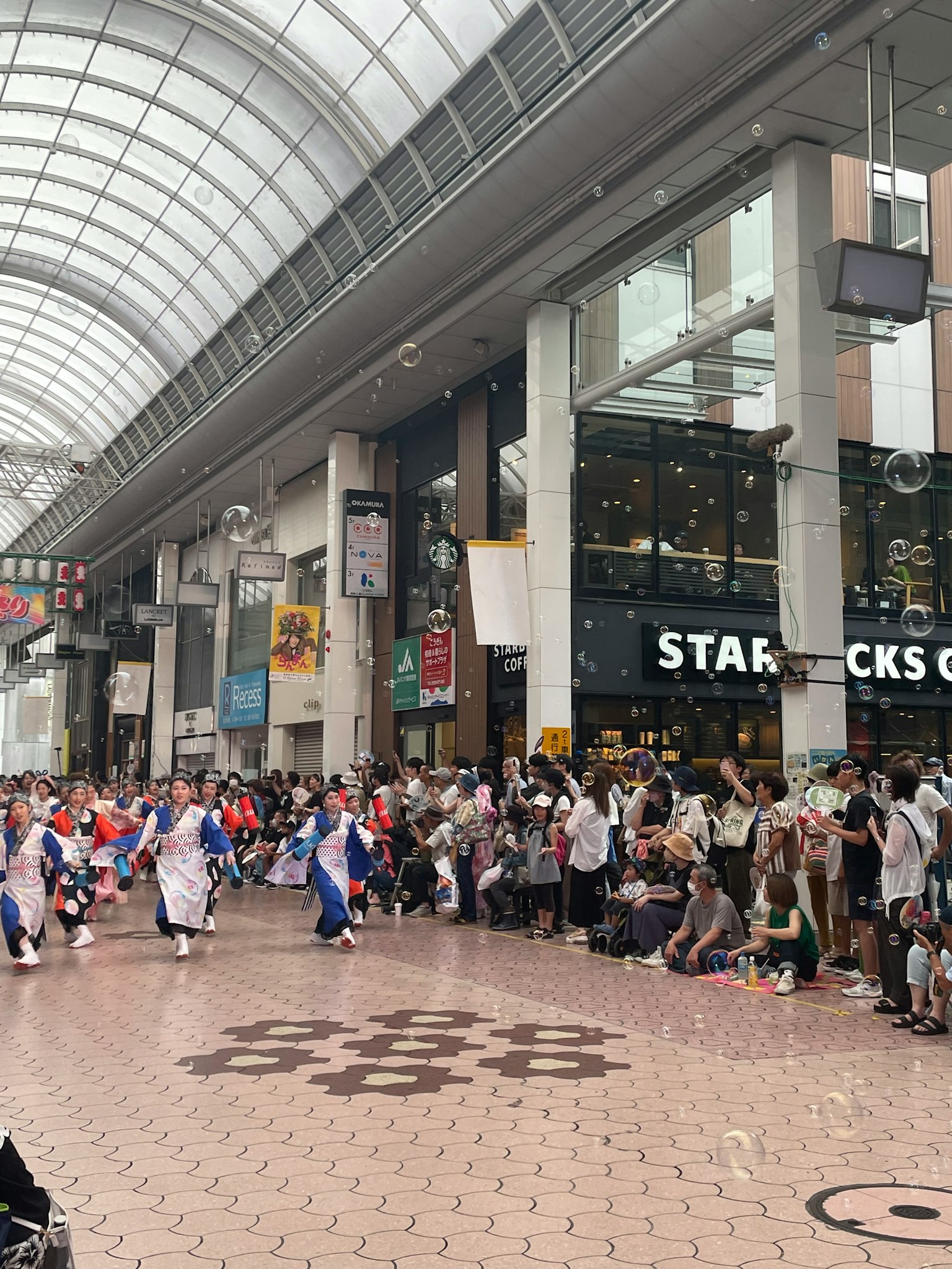 Innenbereich eines Einkaufszentrums mit einer Parade von versammelten Menschen Starbucks-Schild sichtbar