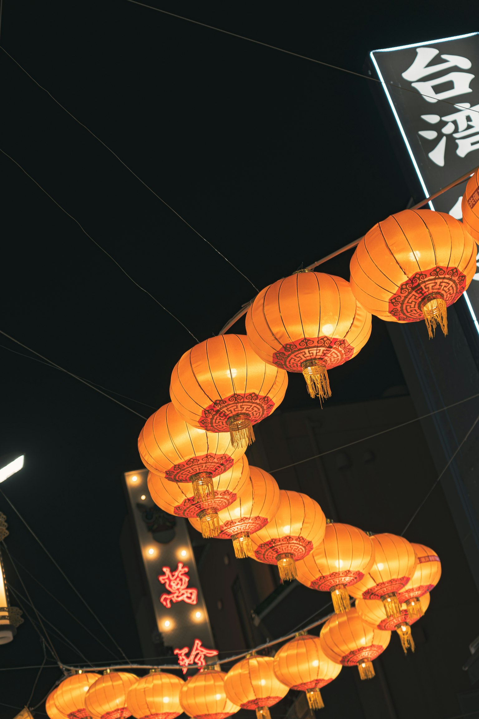 A nighttime view of orange lanterns hanging in a row
